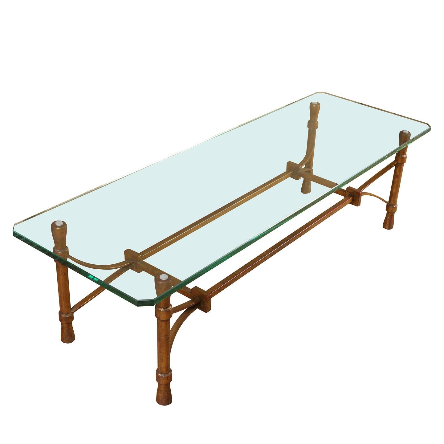 A modernist gilt iron and glass coffee table. The base is constructed of gilt forged iron in modernist style with four cylindrical legs and an open rectangular gilt iron design. The glass top has rounded corners.