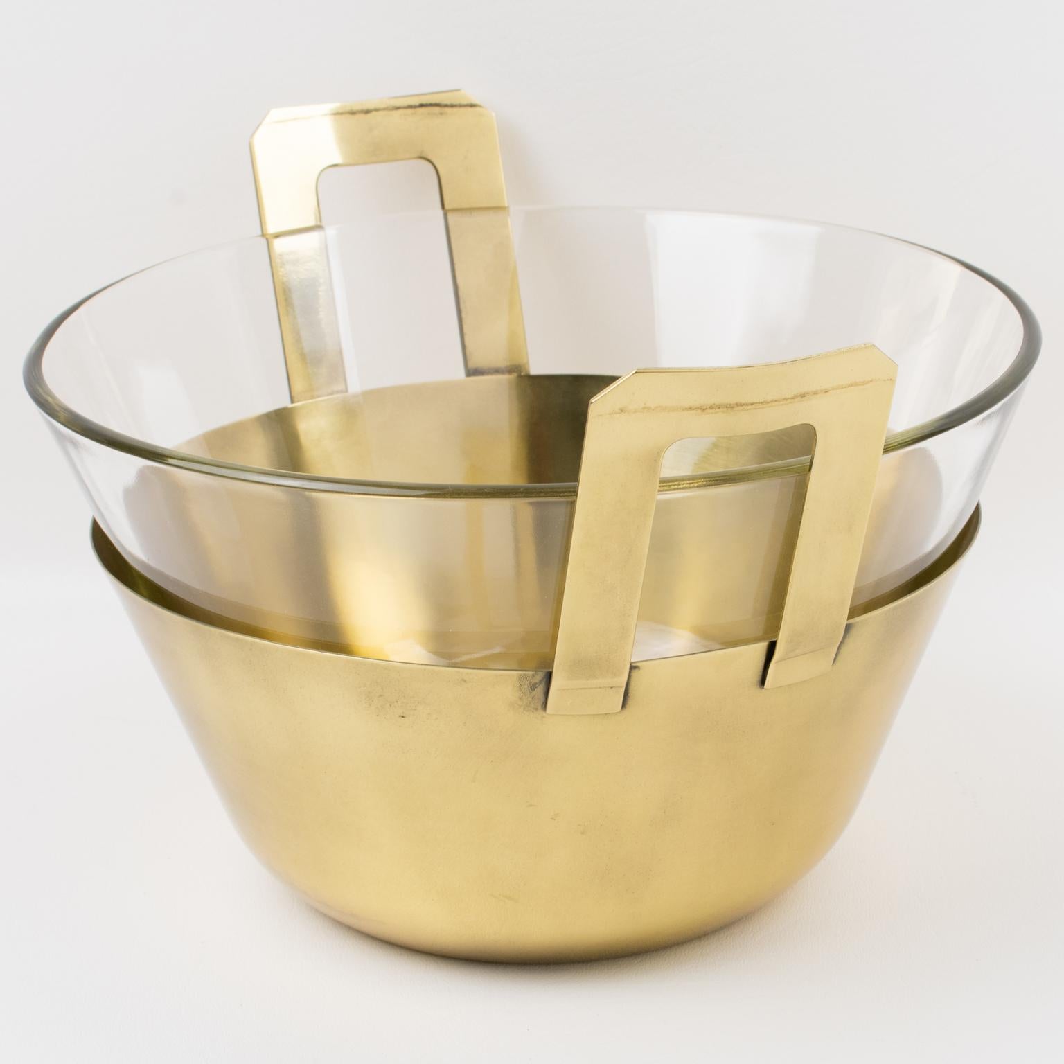 Questa squisita ciotola o centrotavola decorativo in metallo dorato è stata realizzata in Italia nel 1980 circa. Questo pezzo raro presenta una forma arrotondata modernista con un inserto in vetro e alte maniglie in rilievo. Il contenitore di vetro