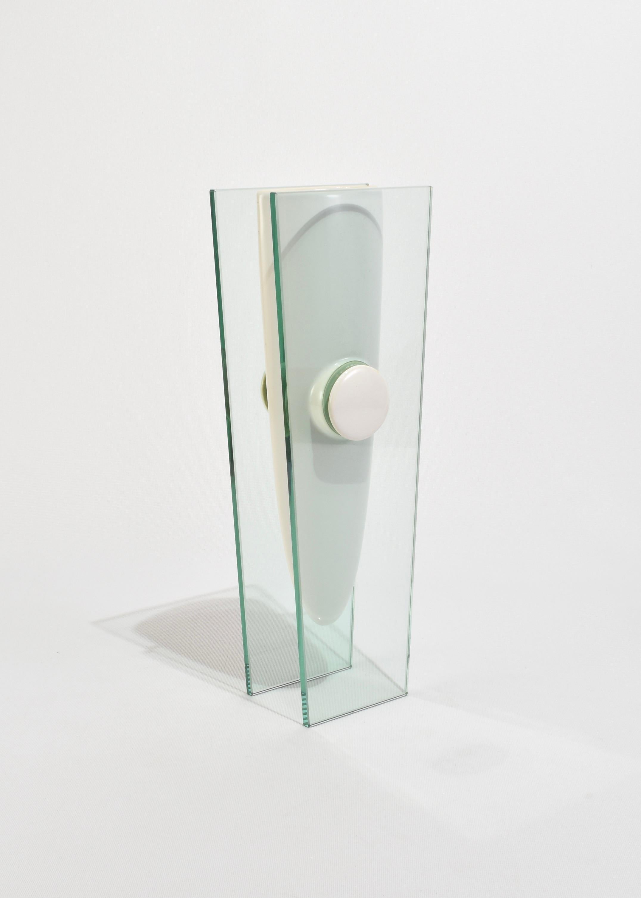 Eine modernistische Vase mit einem länglichen weißen Keramikgefäß, das von zwei parallelen Glasscheiben eingerahmt wird. 
