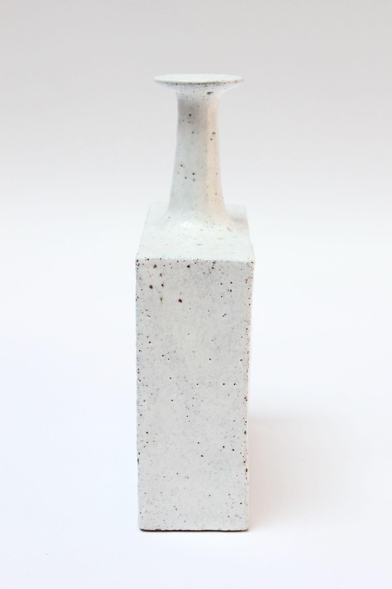 Italian Modern stoneware vase by Bruno Gambone with rectangular base supporting an elegant, tapered neck and flared aperture (ca. late 1950s, Italy). White glaze with specks of turquoise in a few places, as shown. Porous form, giving the piece a