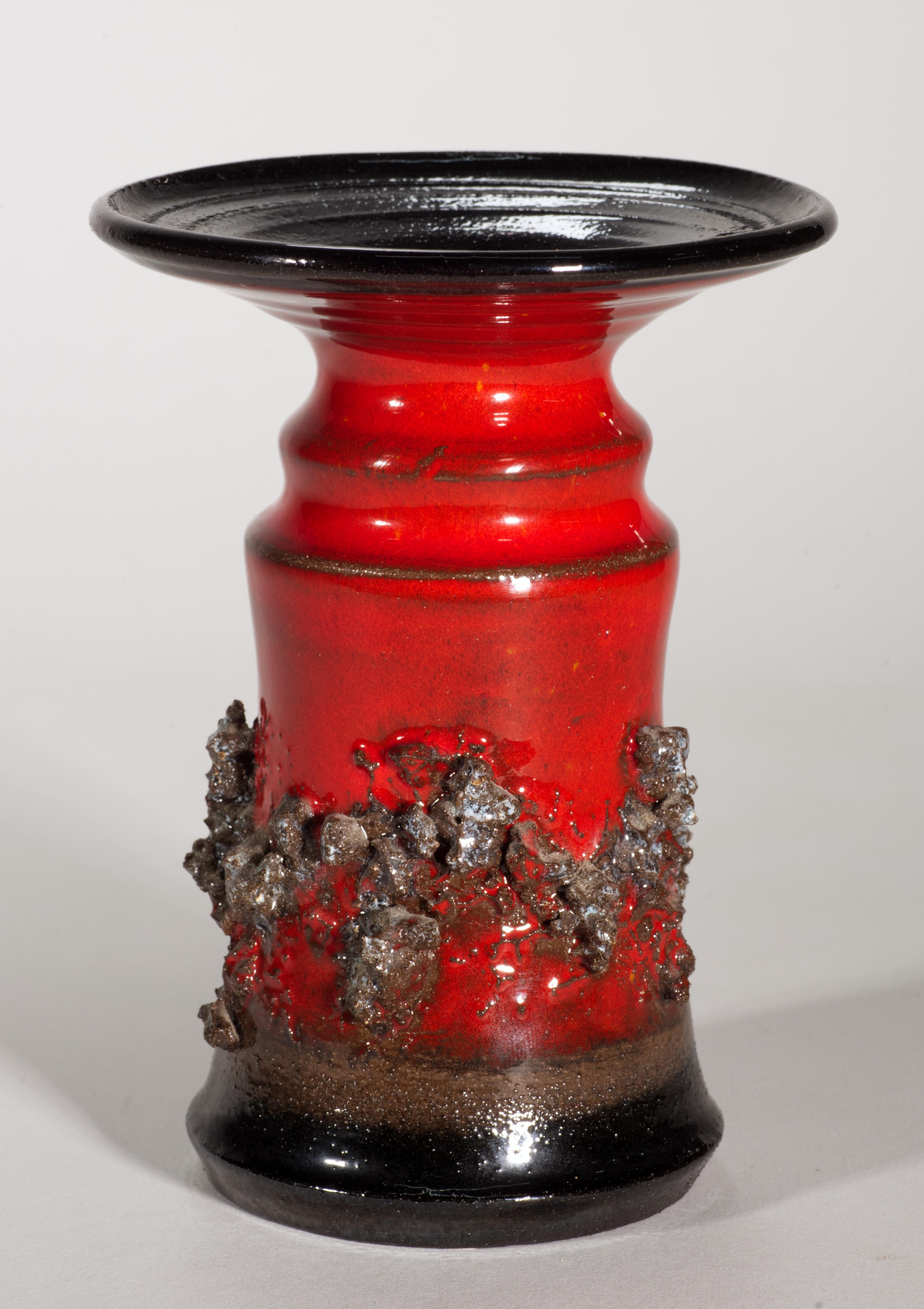  Il vaso scultoreo vintage presenta elementi strutturati in pietra lavica vulcanica applicati a una ceramica lavorata a mano. È stato smaltato a blocchi di colore con smalti rossi e neri lucidi; le superfici interne sembrano non essere smaltate.

Il