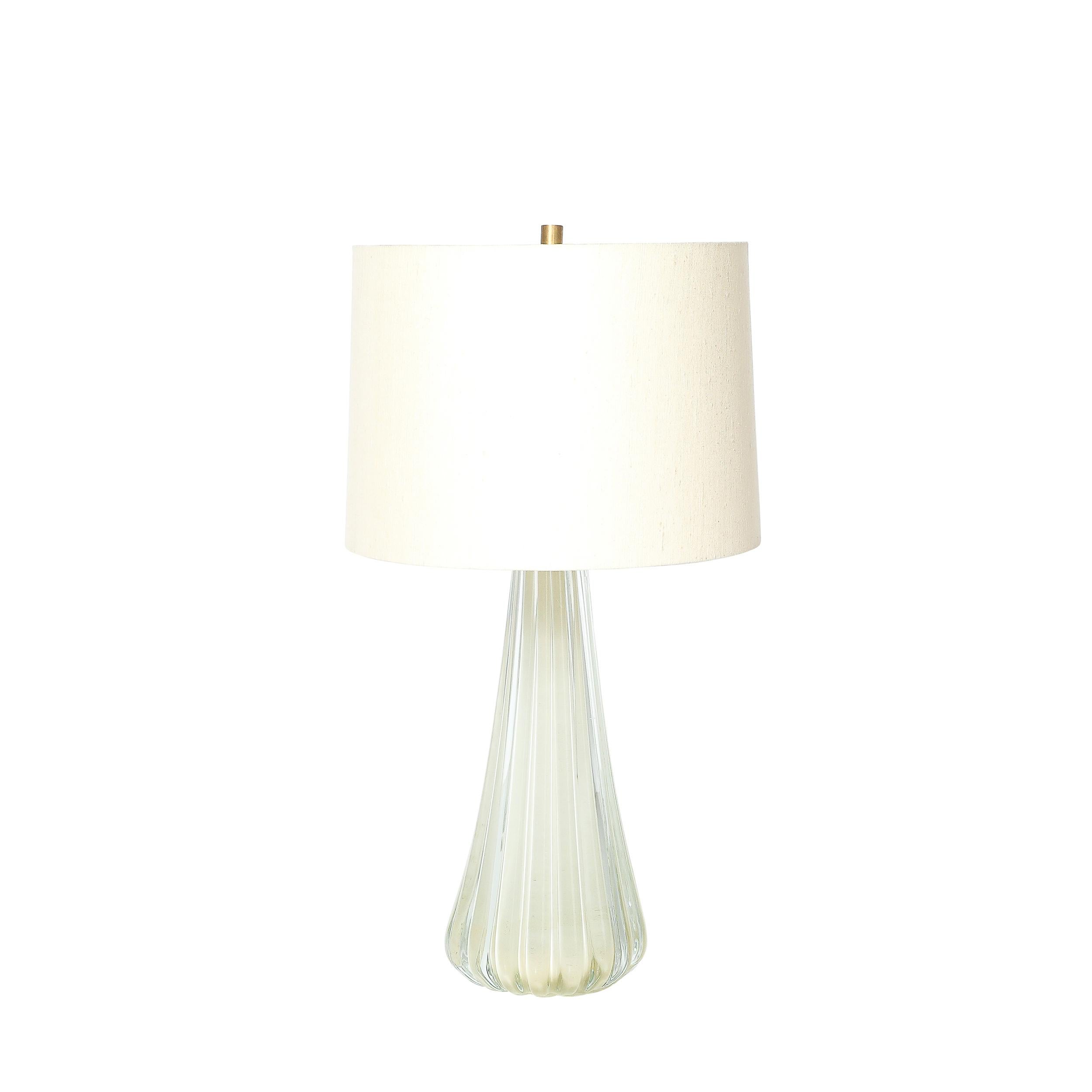 This exquisitely elegant Pair of Modernist Hand-Blown Murano Glass Table Lamps in Oyster W/ Stylized Fluted Detailing originate from Italy during the 21st Century. The lamps feature bodies formed in Hand-Blown Murano glass in a beautiful oyster hue