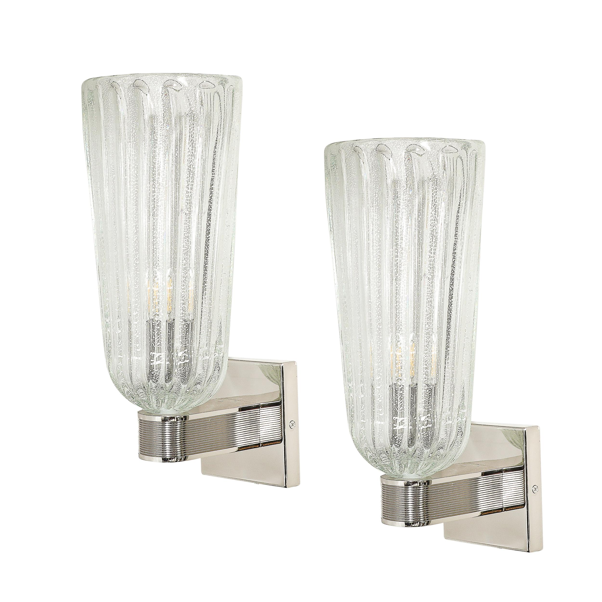 Cette élégante paire d'appliques modernistes en verre cannelé de Murano soufflé à la main, avec des mouchetures en or blanc 24 carats et des Eleg en nickel cannelé, provient d'Italie au 21e siècle. Ces appliques présentent des abat-jours en verre de