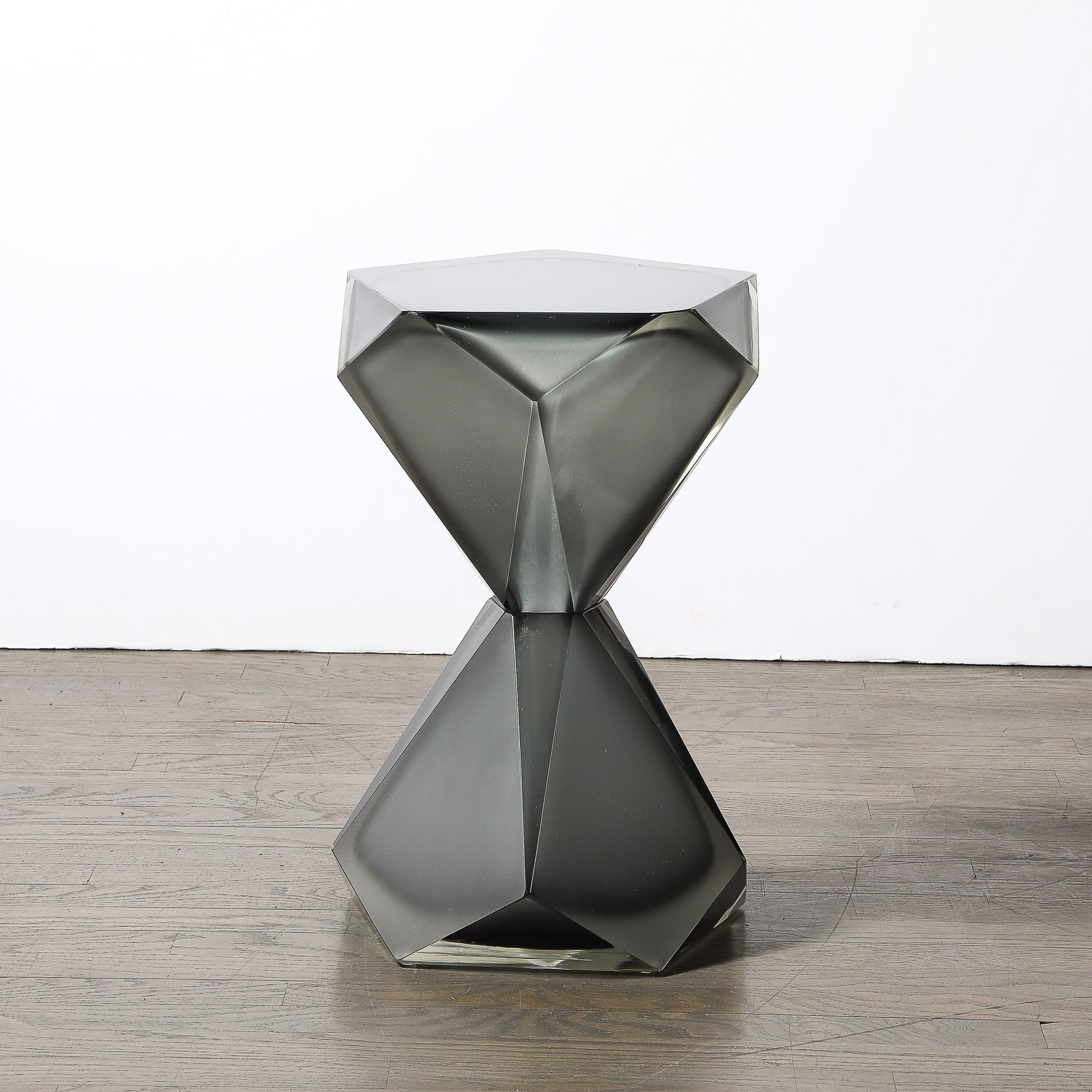 This stunning side/end table exemplifies the artistry of modern Murano glass craftsmanship. Handblown in a sleek faceted hourglass form, the table features a striking smoked graphite hue that transitions into a partially frosted finish, adding