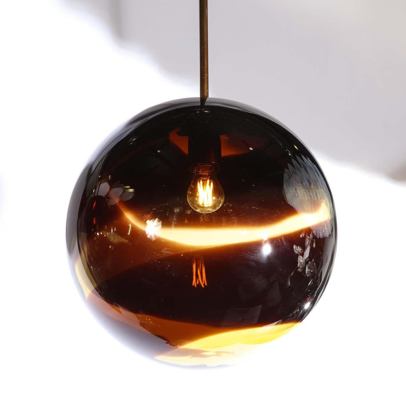 This elegant modernist pendant was handblown in Murano, Italy- the island off the coast of Venice renowned for centuries for its superlative glass production. The fixture offers a spherical body in smoked amber Murano glass with undulating chambord