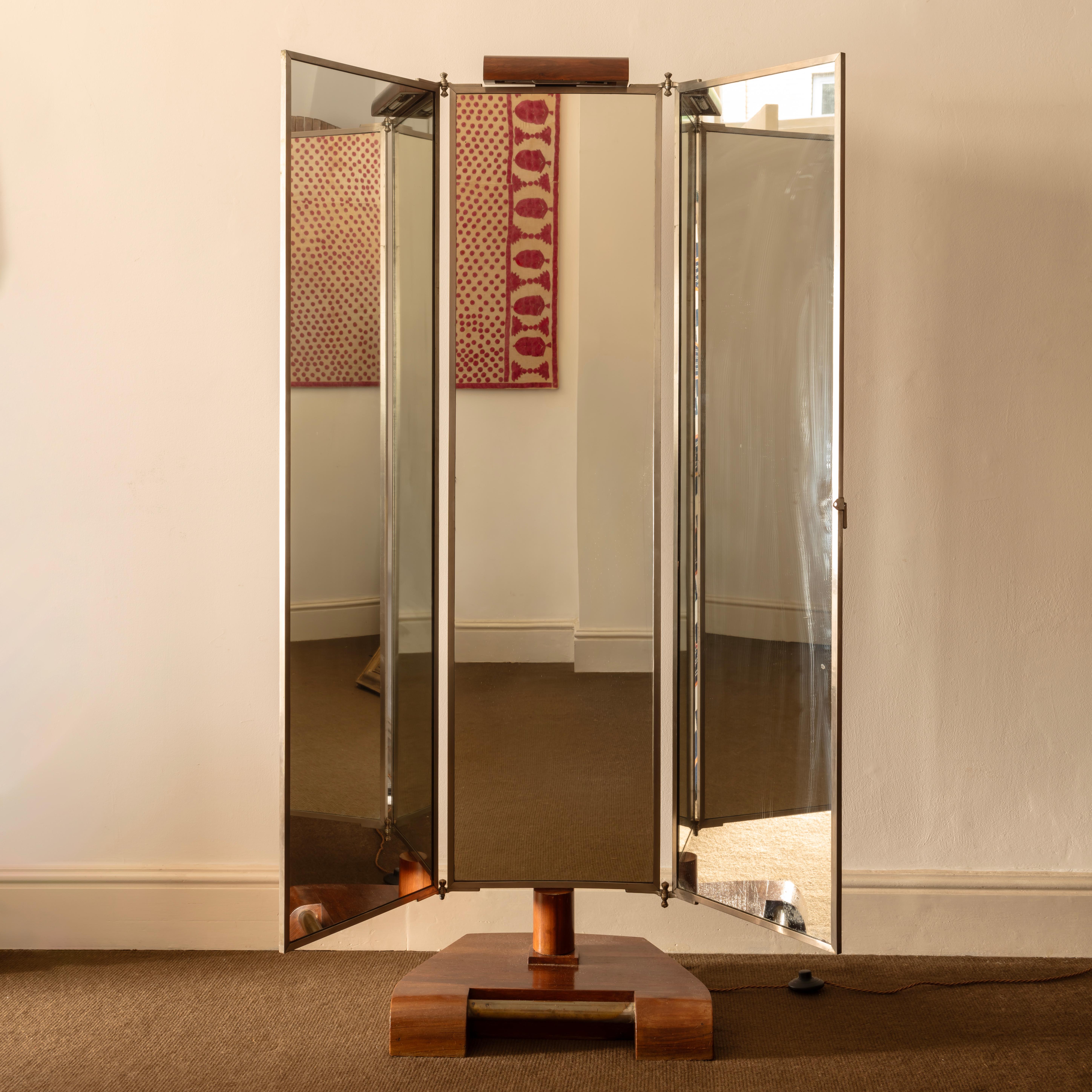 Modernist Illuminated triptych mirror, the three panels fold into one and are finished on the back in rosewood veneer, the stand is mahogany with a brass rail. Cleaned and lightly restored, the lamp is rewired, during restoration a date was found in