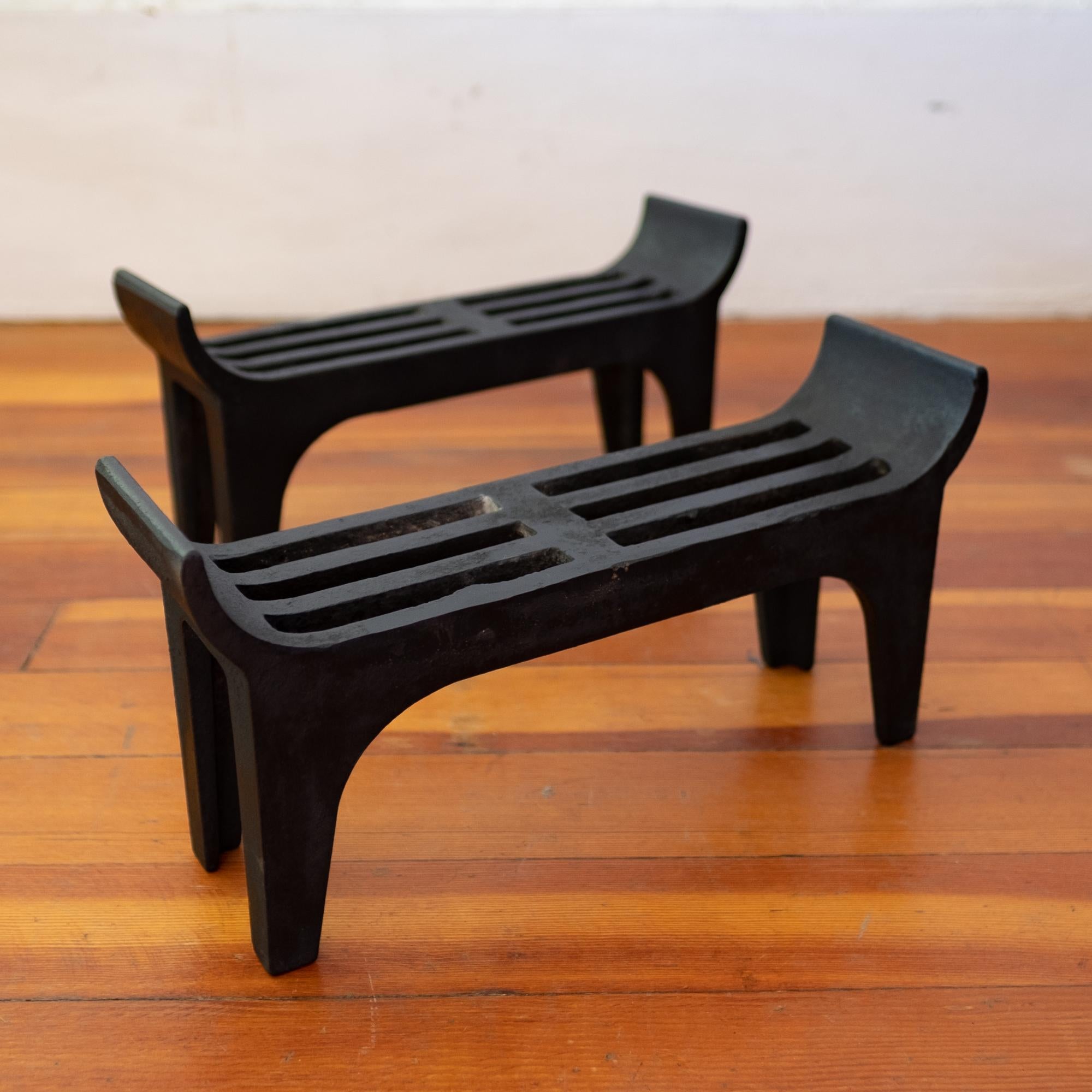 A pair of sculptural Edwin Jackson iron fireplace log holders from the midcentury. The andirons were featured in a 1950 article on fireplace accessories. Edwin Jackson was a high end New York retailer specializing in fireplace furnishings.