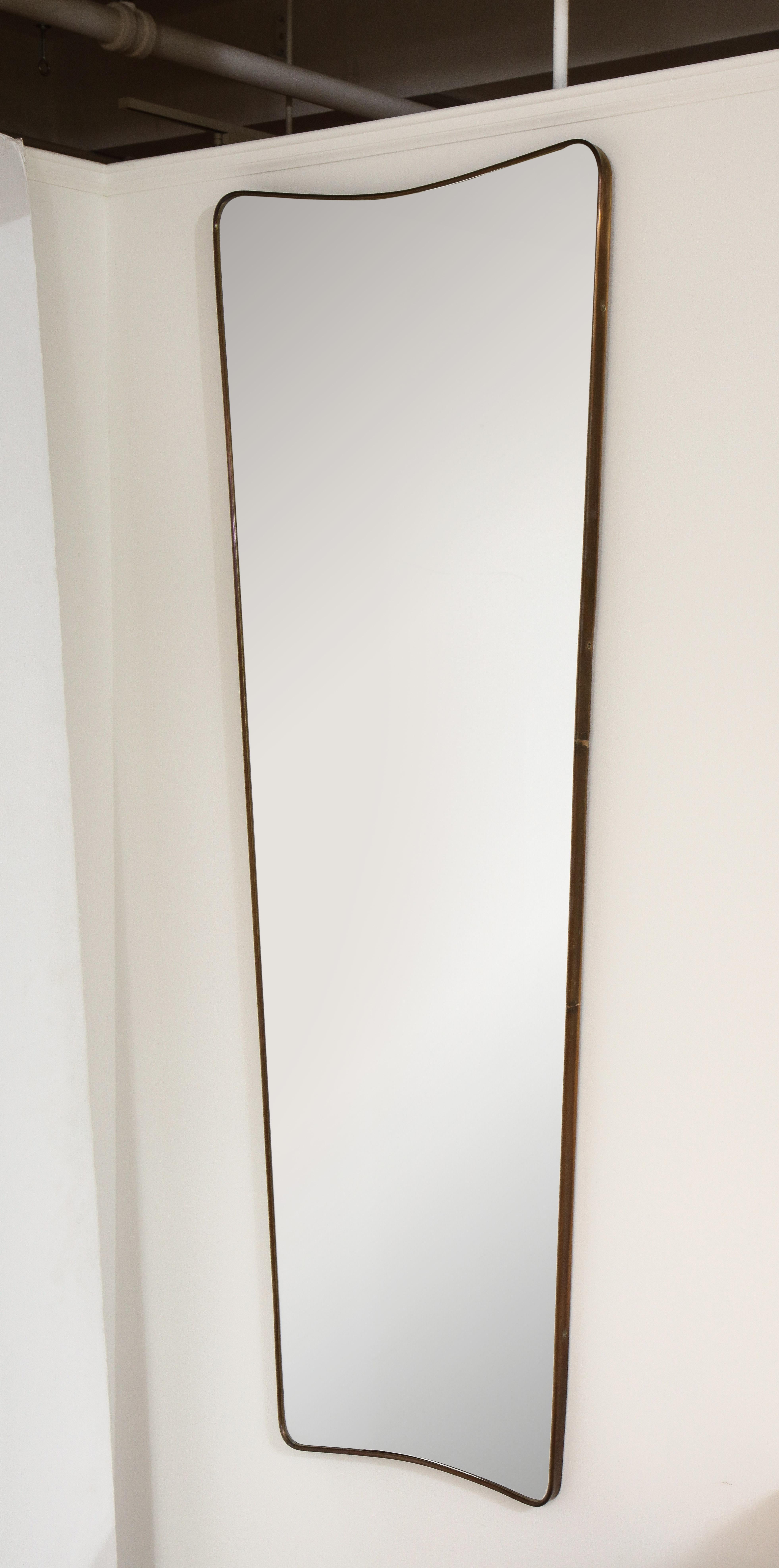 Un miroir moderniste italien en laiton, élégamment allongé et effilé, de grande taille et avec une belle patine d'origine en laiton. Le sommet présente un arc simple, repris également à la base. Ce design italien très simple et classique s'adapte à
