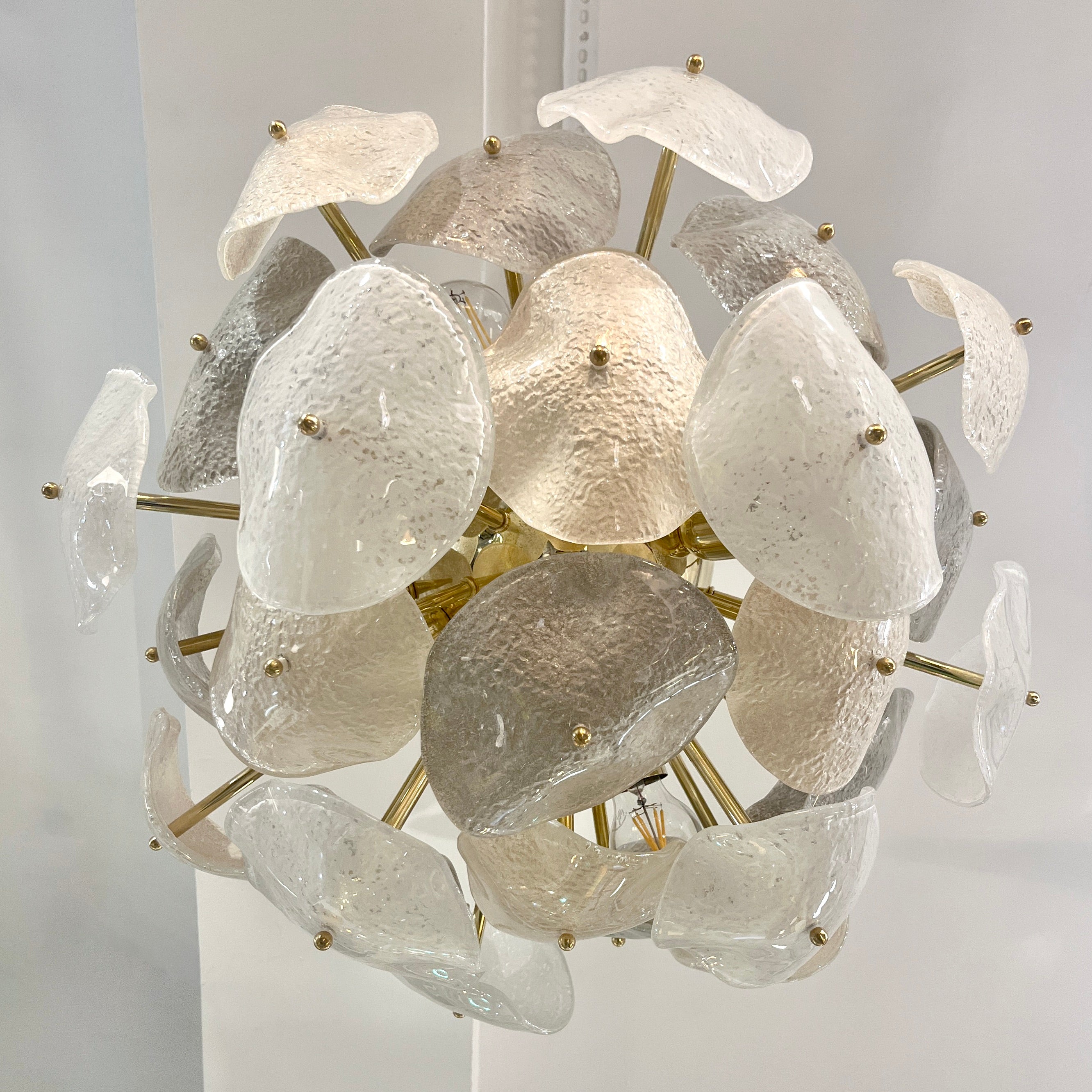 Contemporary bespoke Venetian post modern chandelier with sunburst organic design and Hollywood Regency glamour, entirely hand crafted in Italy, composed of a sensual amorphous cluster of interlocking curved concave leaves in Murano glass worked in