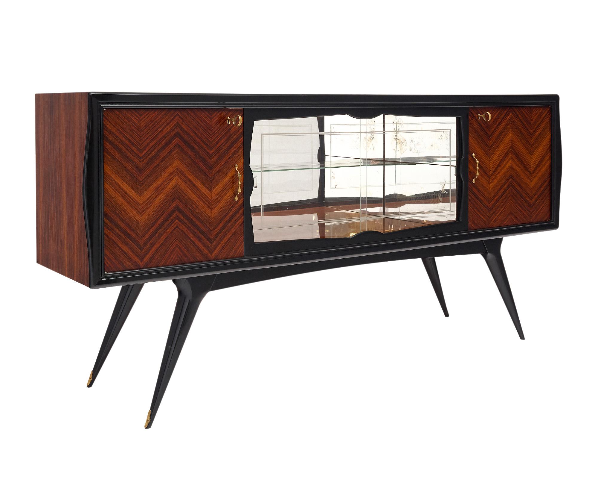 Modernist buffet from Italy. This piece has the iconic flared legs a chevron pattern to the rosewood façade. The two doors open outward to interior shelving, while the center section of the buffet forms the bar, adorned by two glass sliding panels.
