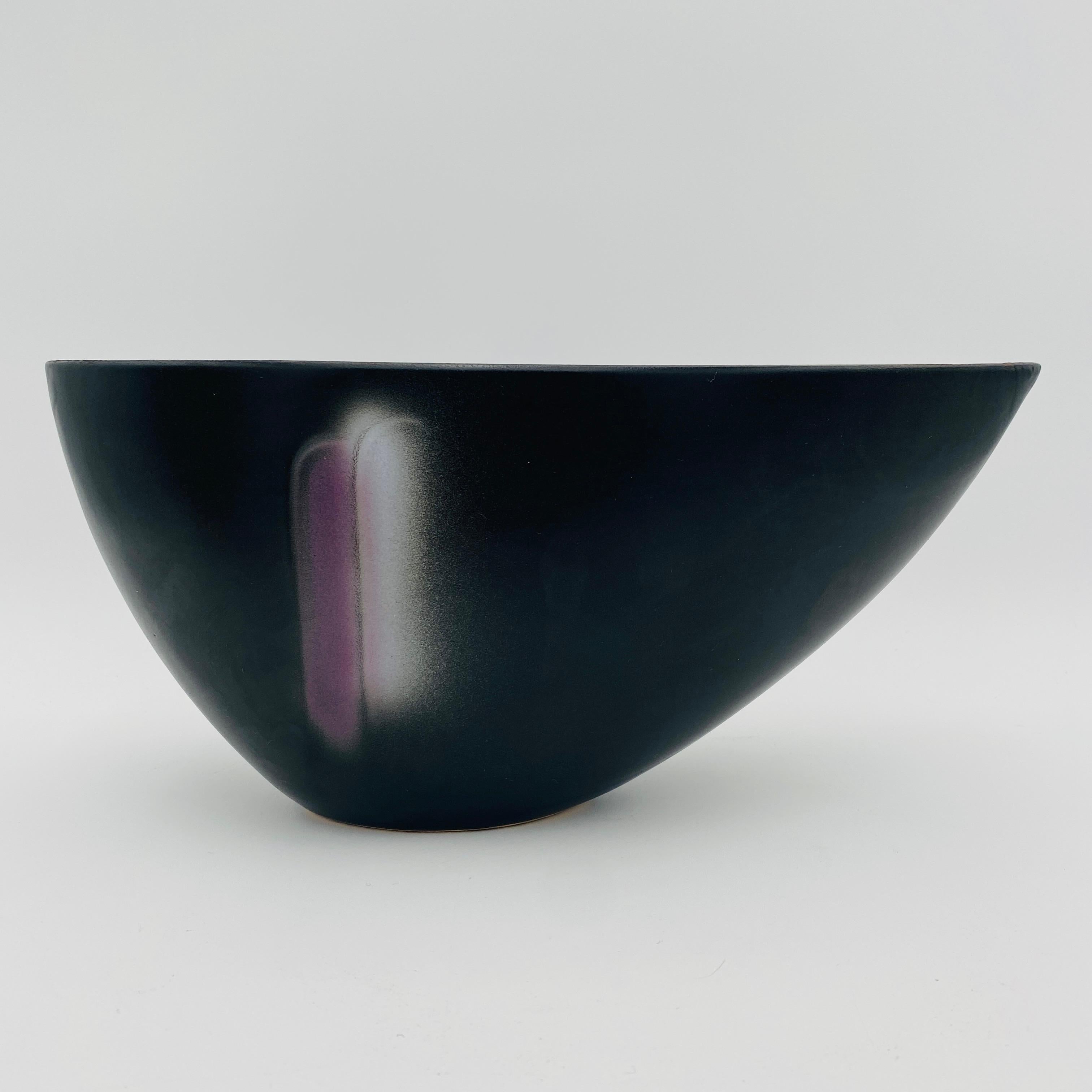 This is a minimalist Japanese pottery ikebana vase, circa the 20th century. The elongated asymmetrical shape is very biomorphic. The vase has a semi-gloss black glaze with a pop of purple and white glaze color that almost looks spray painted onto