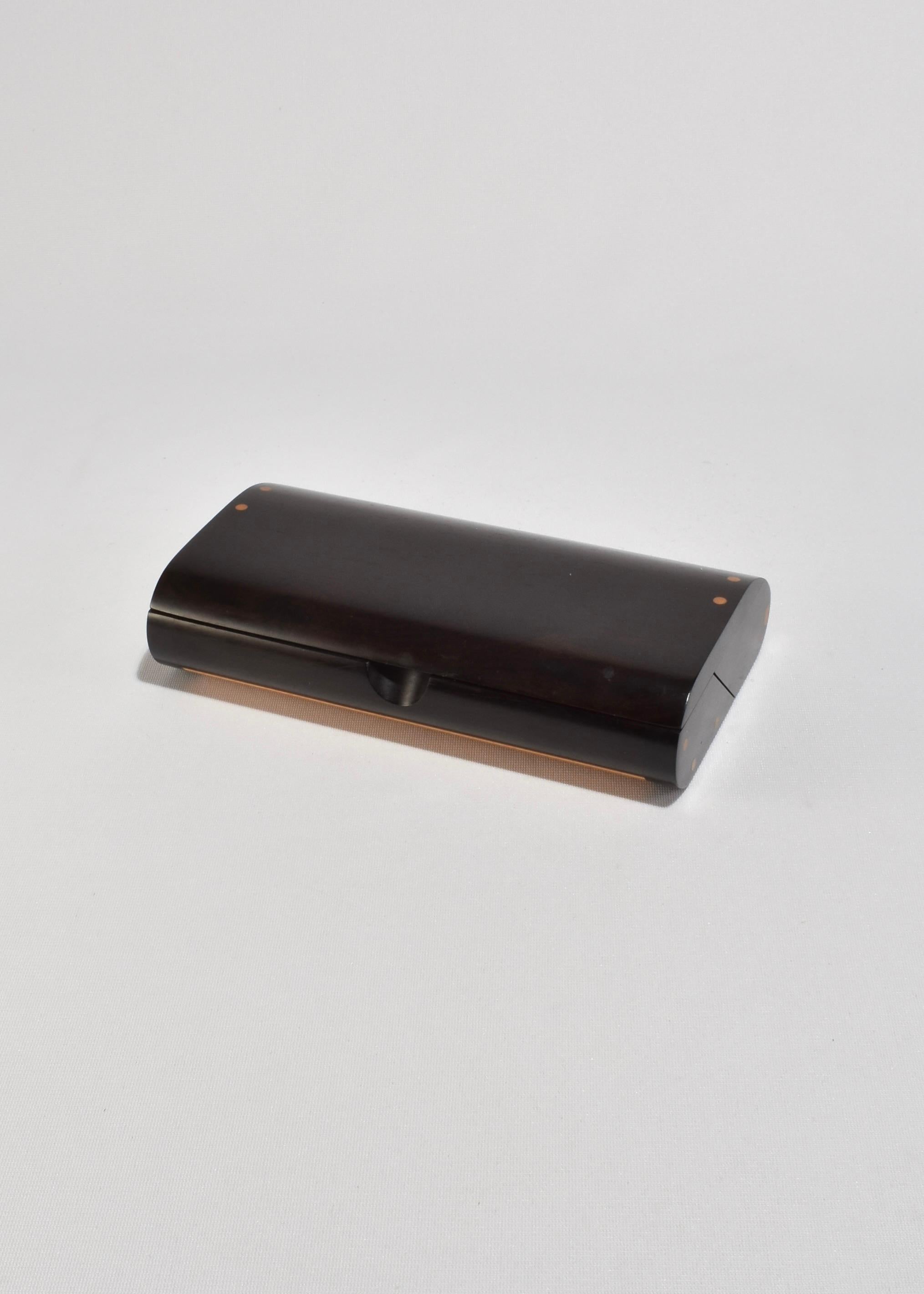 A sculptural modernist jewelry box with a curved rosewood lid and inset side hinges. The handcrafted design features dovetail-like joinery at the corners and a smoothly contoured profile. Opens to a black velvet-lined interior with warm wood