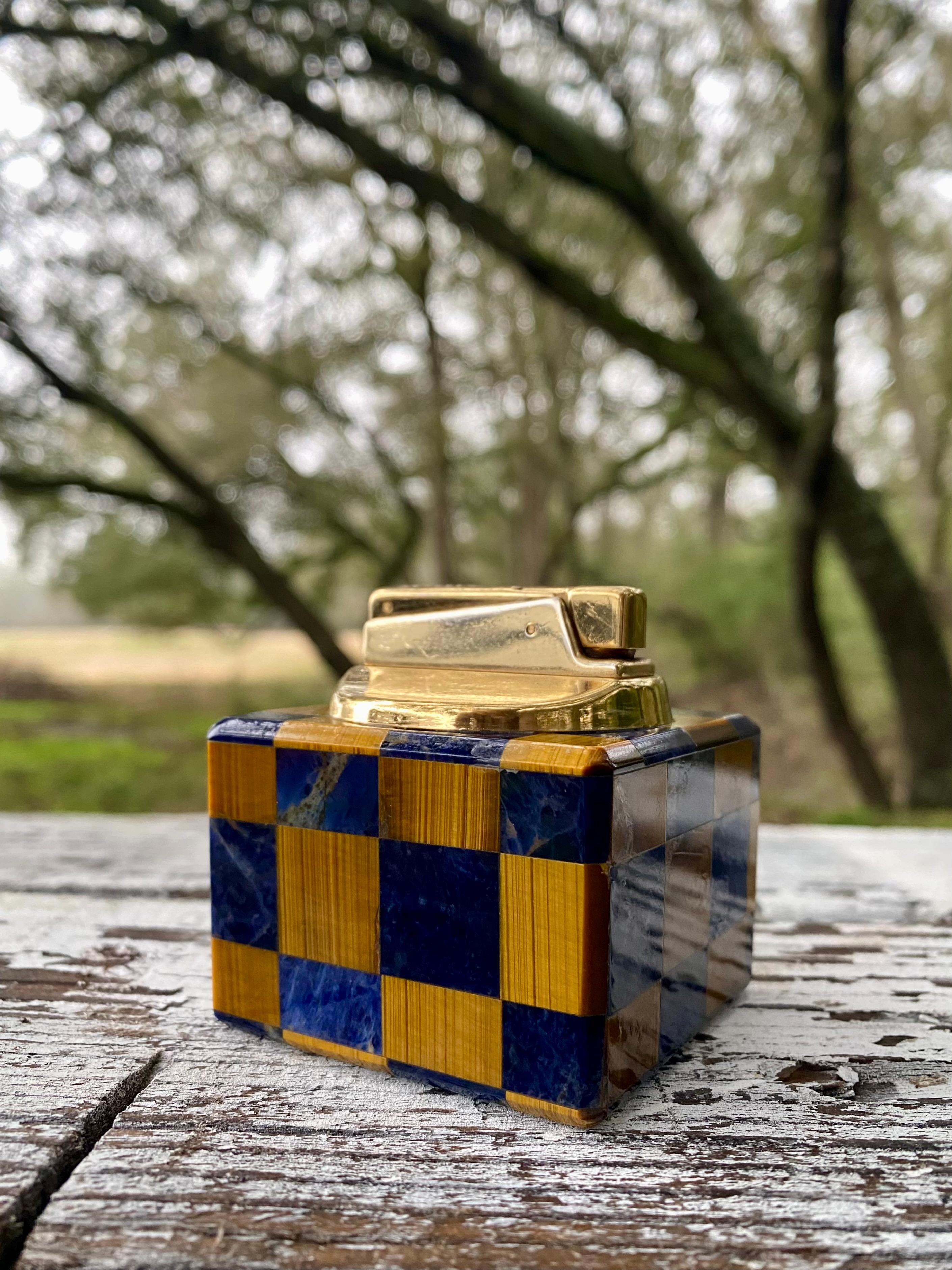 Presenting a rare Midcentury Modern gemstone lapis lazuli and tiger eye desk lighter, a supreme luxury object that was created to highlight and show off the craftsmanship of the era.

This cube shape object glows in blue and iridescent brown