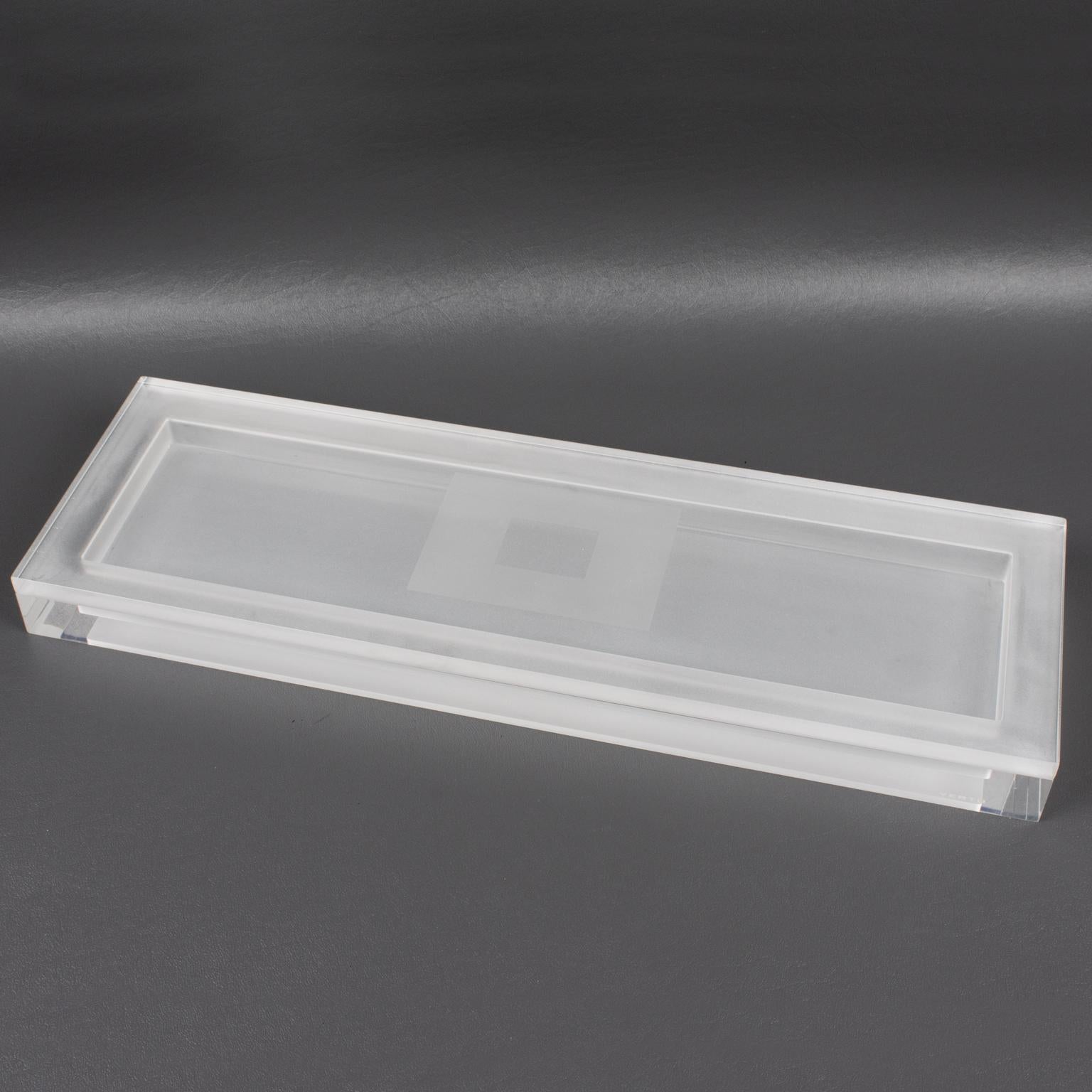 Esta caja modernista con tapa de los años 80 está hecha de Lucite. Esta impresionante pieza presenta una forma rectangular extra larga y plana con un intrincado diseño geométrico transparente y esmerilado. El lateral está marcado con el logotipo