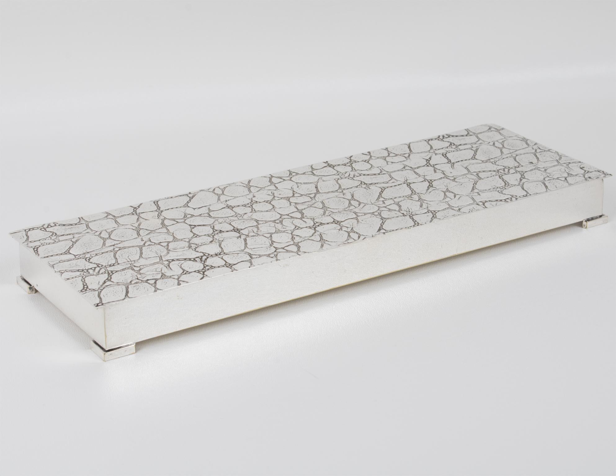 This extraordinary modernist silver-plated covered box, crafted in France circa 1960, is a true testament to elegance and refined craftsmanship. Its elongated, flat silhouette embodies minimalist sophistication, while the exquisitely embossed,
