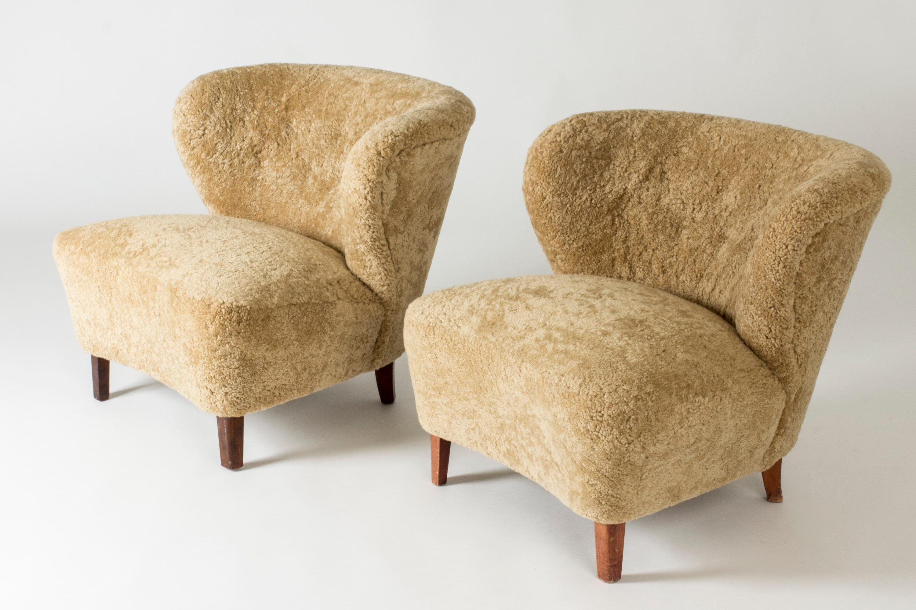 Pair of elegant lounge chairs by Gösta Jonsson, upholstered in caramel colored sheepskin. Chunky design with generous lines.