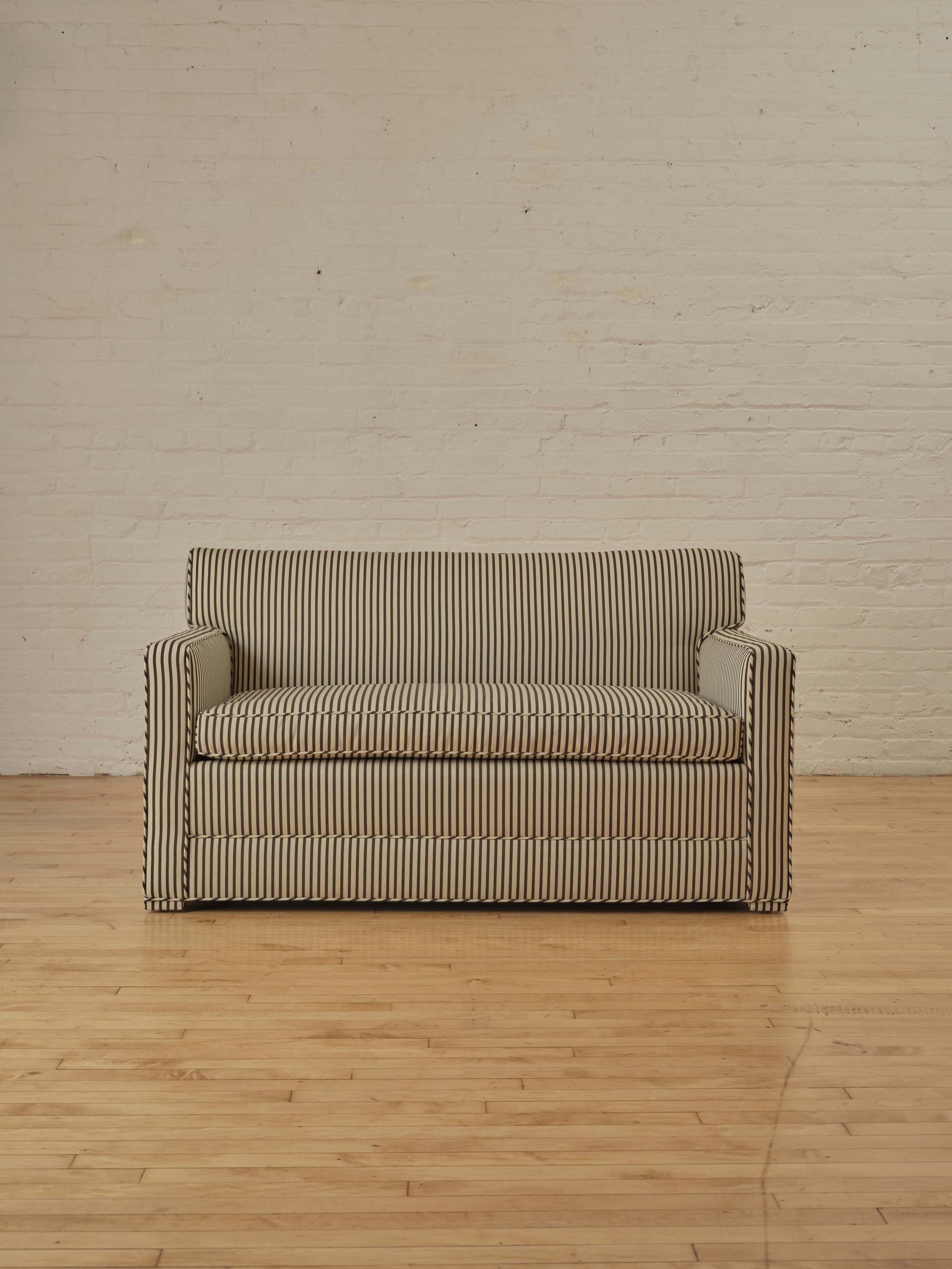 Modernist loveseat reupholstered in Dedar Milano's, Strange Love fabric in chocolate and ivory stripe pattern with a matching piping detail. The loveseats compact design makes it an ideal choice for both small and spacious living spaces.