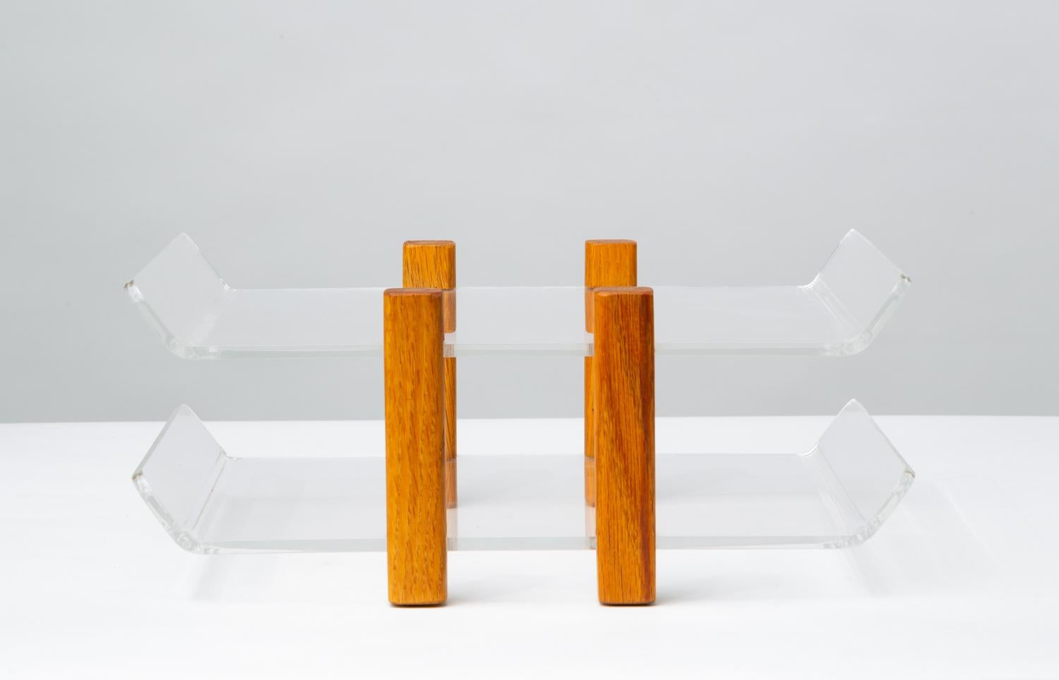 A simple paper tray with lucite in and out shelves separated by notched posts of solid oak. Each shelf is raised at the edges to keep papers in place. The four posts are square with rounded edges, and a central peg keeps the shelves in