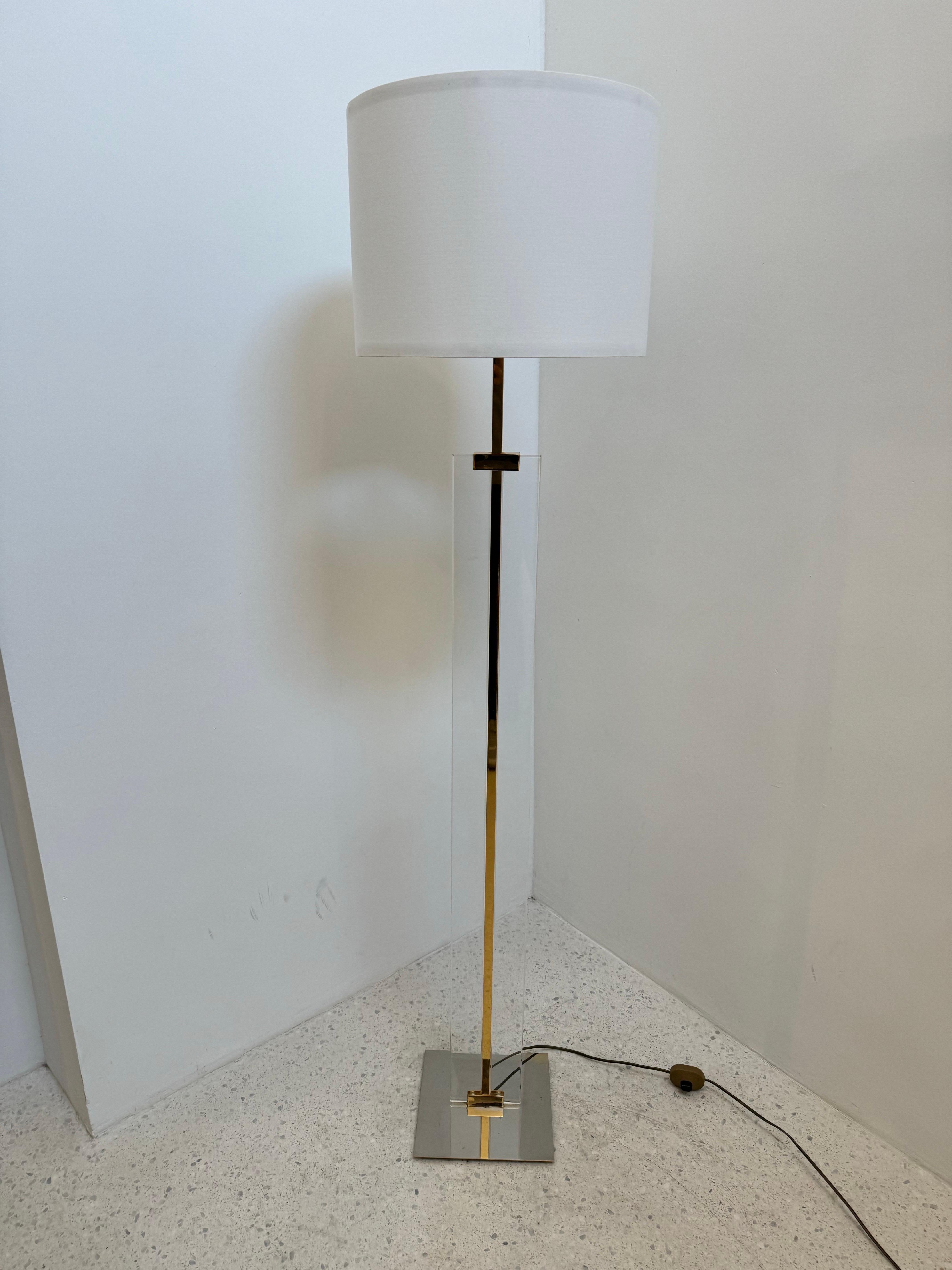 Elegant 1970s floor lamp featuring a striking combination of clear lucite, polished brass, and chrome. The sculptural stem rises from a squared chrome base, with a brass inlay detail and lucite column creating a sleek, floating effect. Topped with a