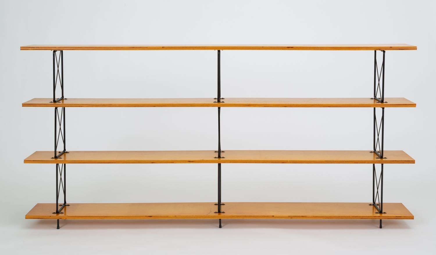 A versatile shelving or display unit with long mahogany plywood shelves and a framework in black-enameled steel. Each of the three wooden shelves is supported by three wire brackets with an X-shaped brace. The piece sits atop six small feet, capped