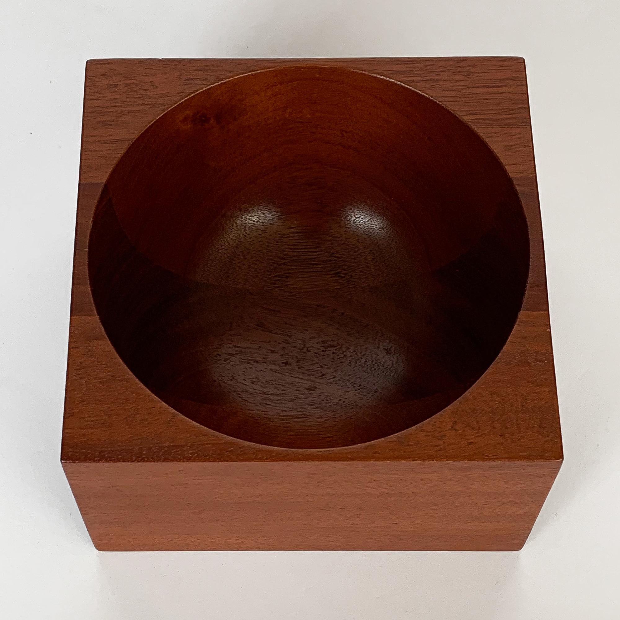 Modernist turned solid mahogany wood bowl by John Sage. Inspired by Poul Kjaerholm's marble PK-Bowl. Square form with concave half circle bowl. Inscribed: Bear Woodworking, John A. Sage, 1982. The original label states mahogany desk bowl.
 