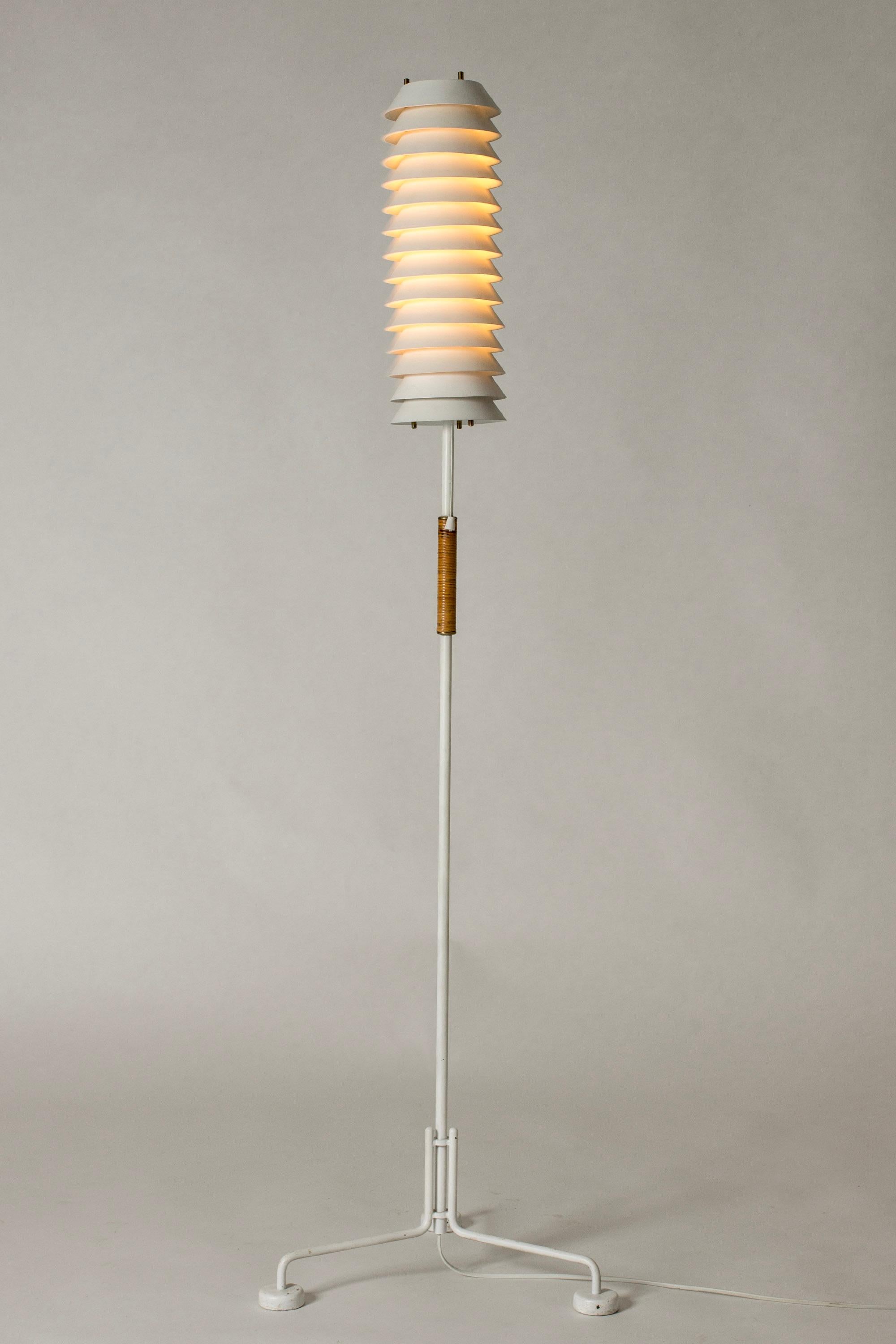 Striking “Maija Mehiläinen” (“Maija the Bee”) floor lamp by Ilmari Tapiovaara. Stacked white lacquered lamellas let out a soft light, contrasting industrial looking base. Rattan detail on the stem.