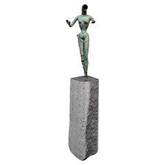 Escultura metálica modernista de una forma femenina fijada sobre una torre de granito
