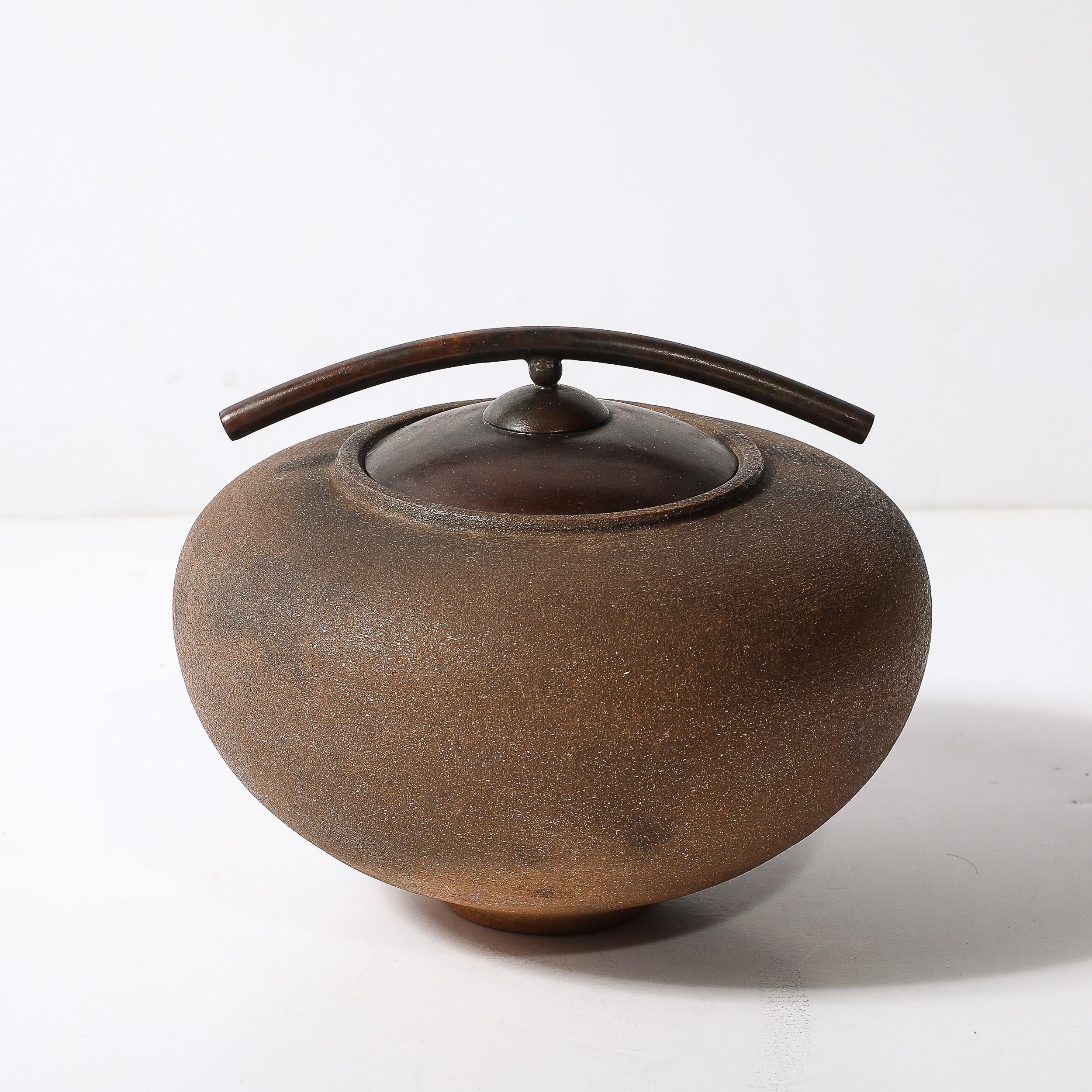 Questo sorprendente vaso modernista, realizzato a mano in argilla mica e cotto a fumo, mette in mostra l'innovativa arte della ceramista americana Carol Green. Realizzato nel 1985 circa, il pezzo presenta un esclusivo coperchio in bronzo patinato,