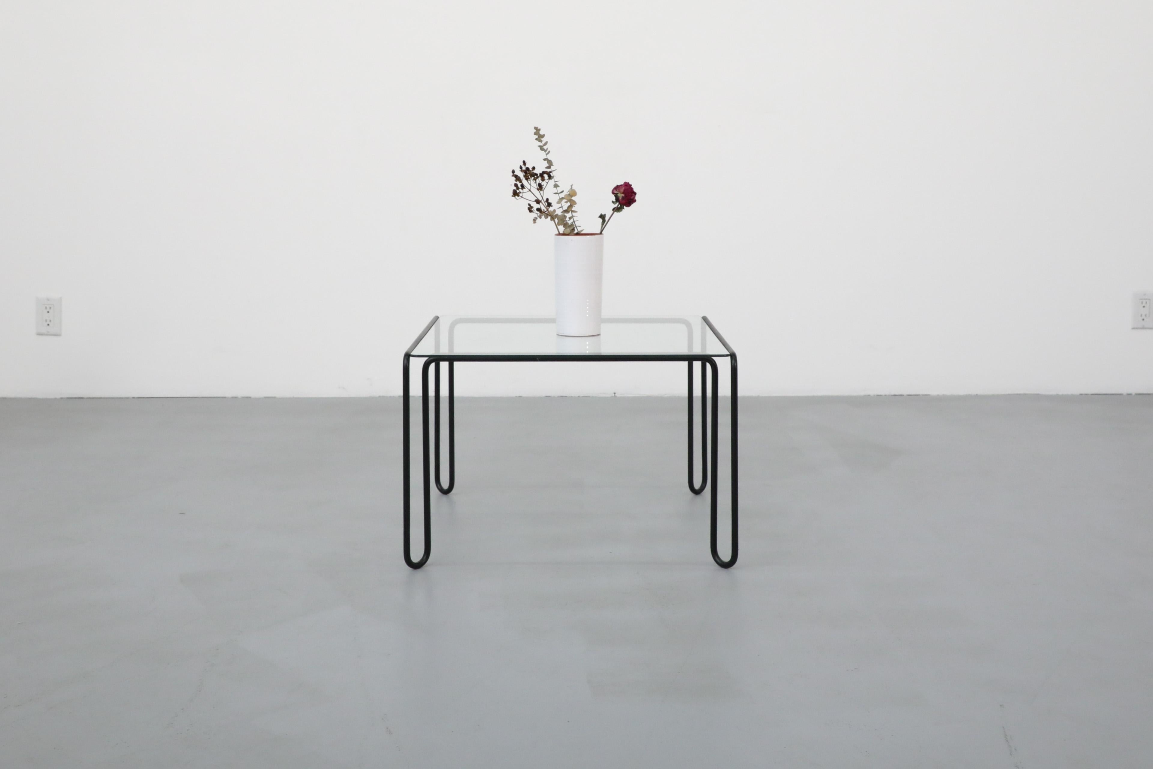 Table basse carrée de style Mid-Century Modern avec plateau en verre et structure en métal tubulaire plié revêtu de poudre noire. En état original avec une usure visible correspondant à son âge et à son utilisation. Montrée avec la table basse