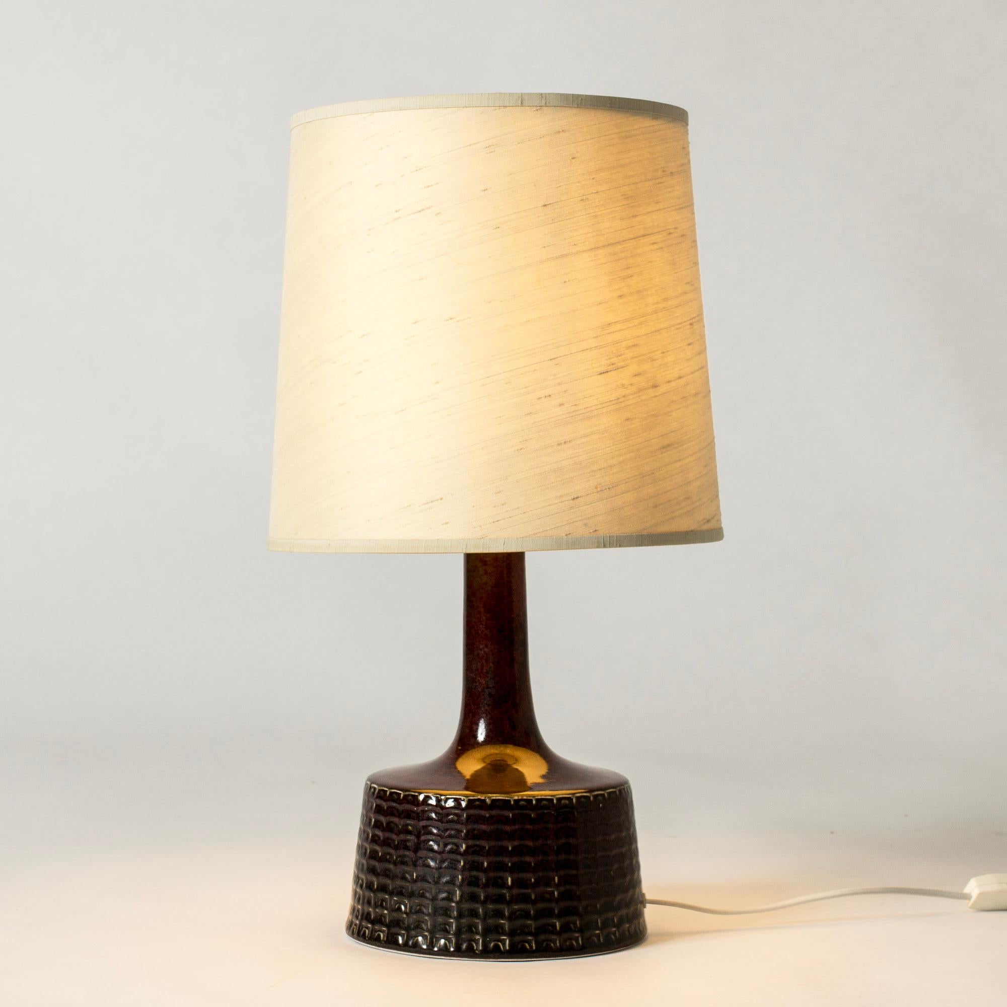 Cool table lamp by Stig Lindberg, with a stoneware base embossed with a graphic pattern and glazed dark red. Original raw silk shade.
