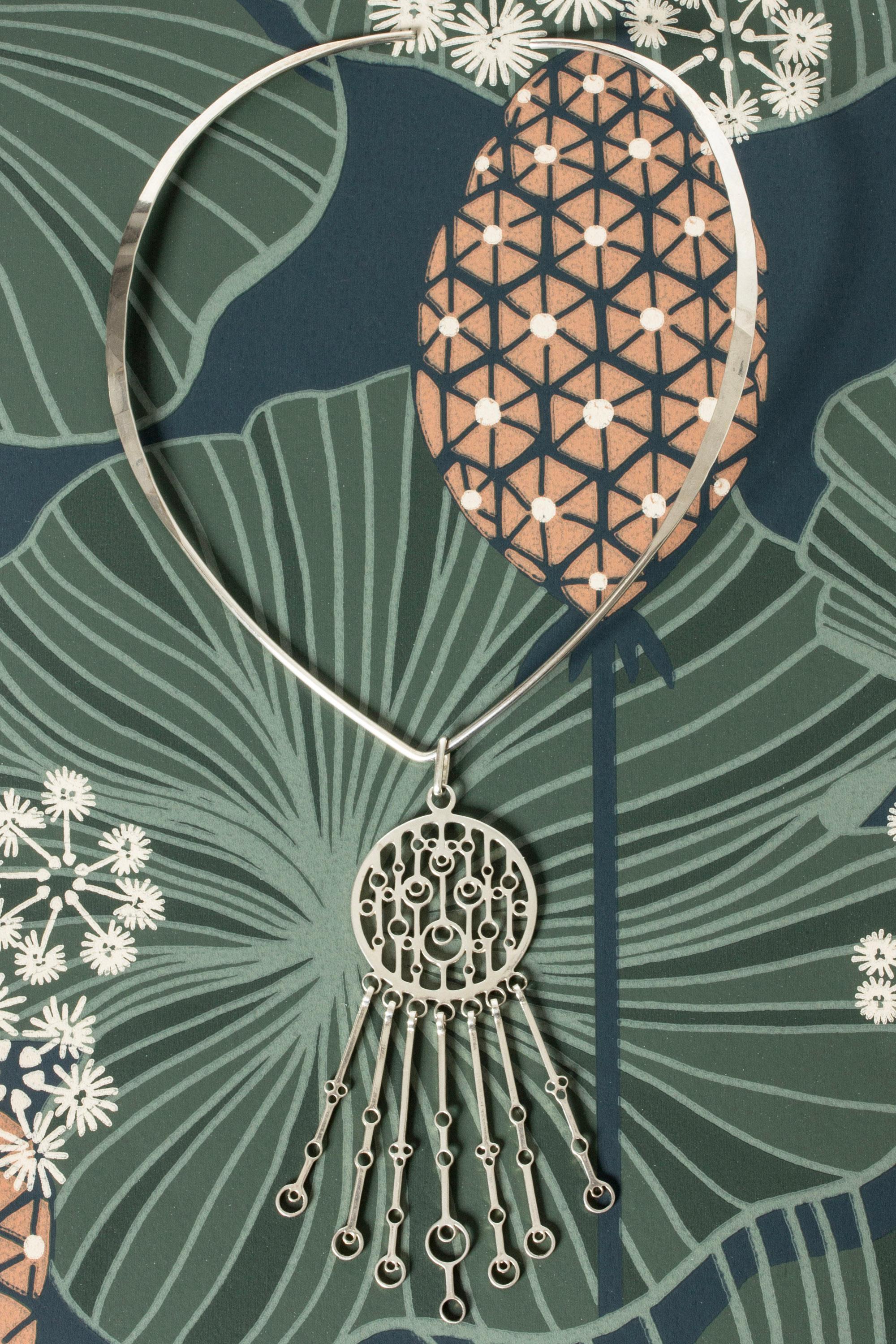 Beautiful silver neckring by Marianne Berg, with a large kinetic pendant in a folkloristic design. Looks great with a plunging neckline or with a open shirt.