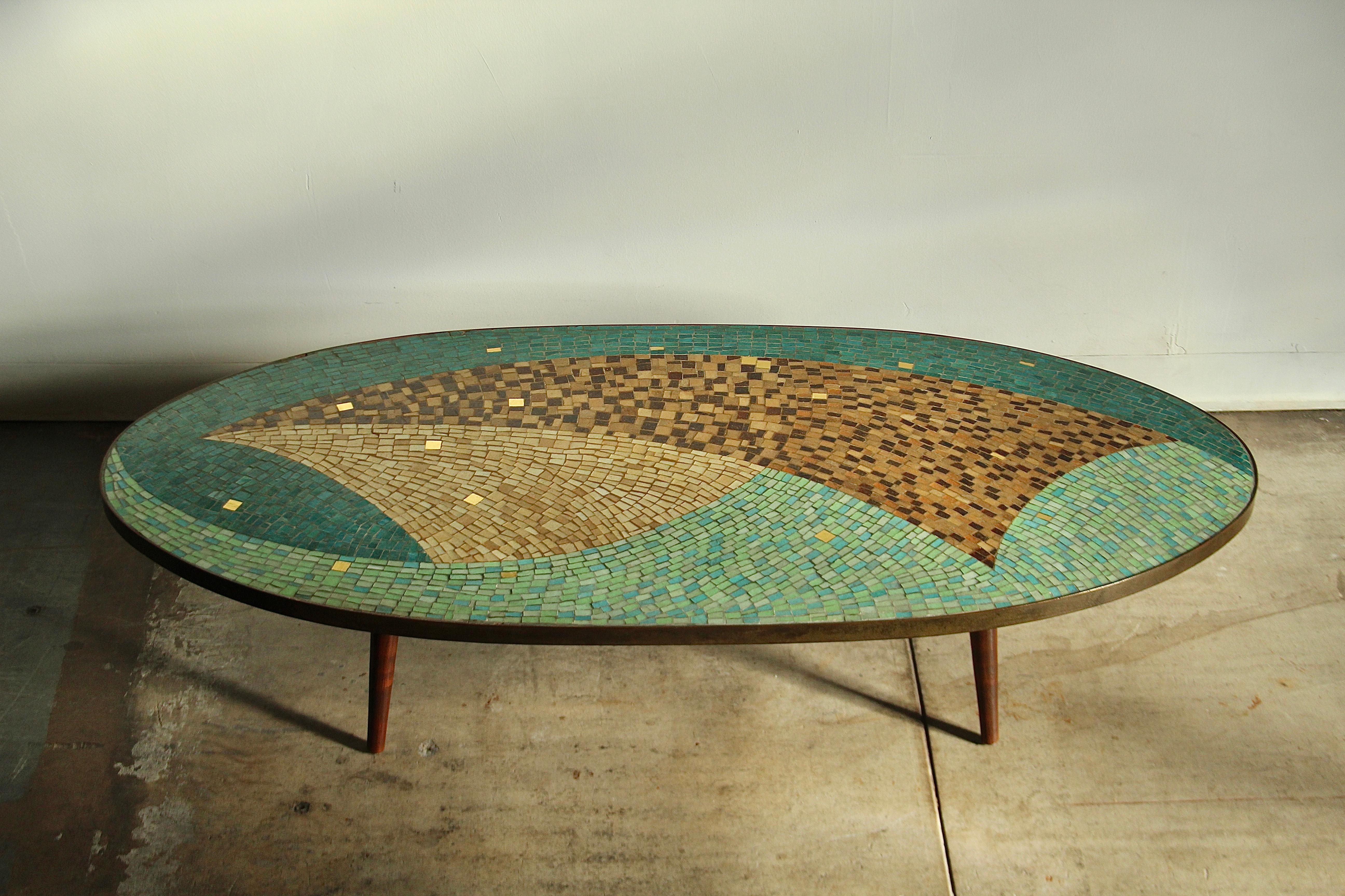 Une superbe table basse en mosaïque, unique en son genre, fabriquée au début des années 1960, peut-être par Jack Boyd. La grande table ovale présente un impressionnant plateau en verre vénitien dans différentes nuances de bleus, de verts, de bruns