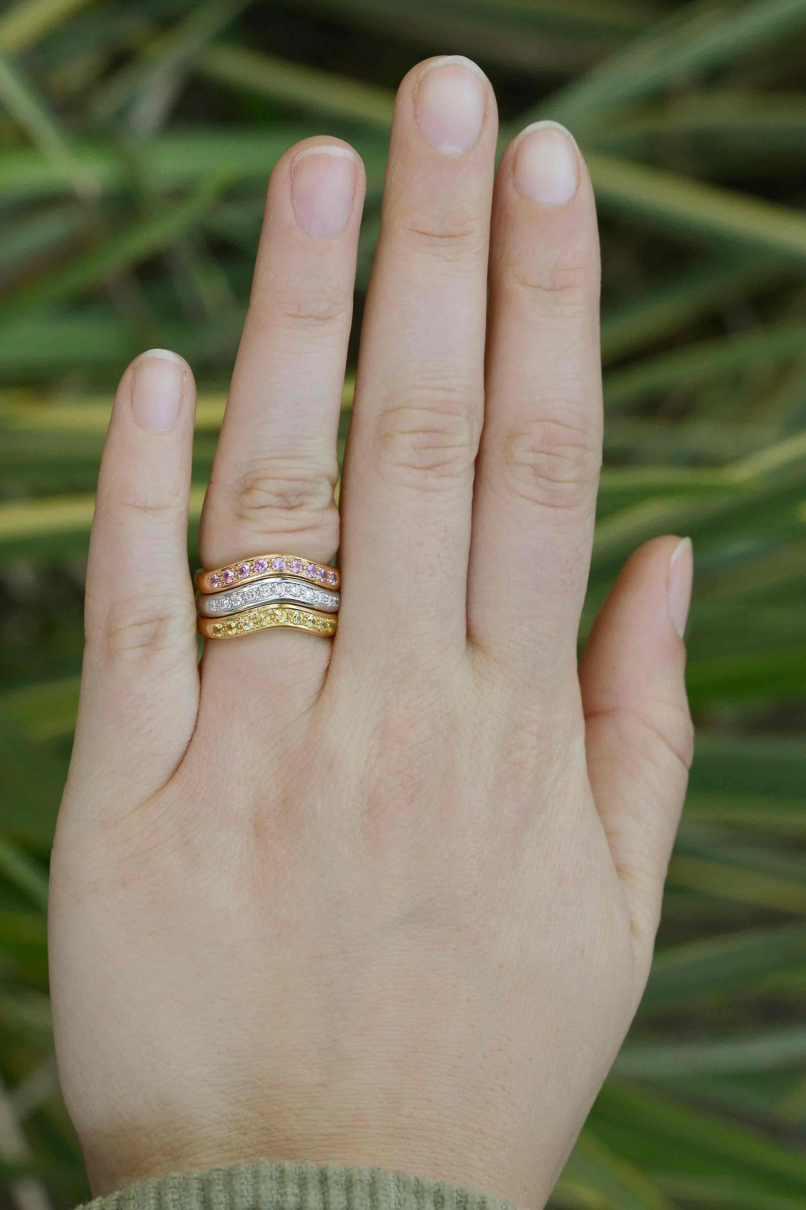 A gorgeous, curved 3 band trinity ring wedding band. Featuring an array of tri color golds, this ring is the perfect accompaniment to your other favorite pieces. A triple row of pink and yellow sapphires and diamonds are smartly placed into