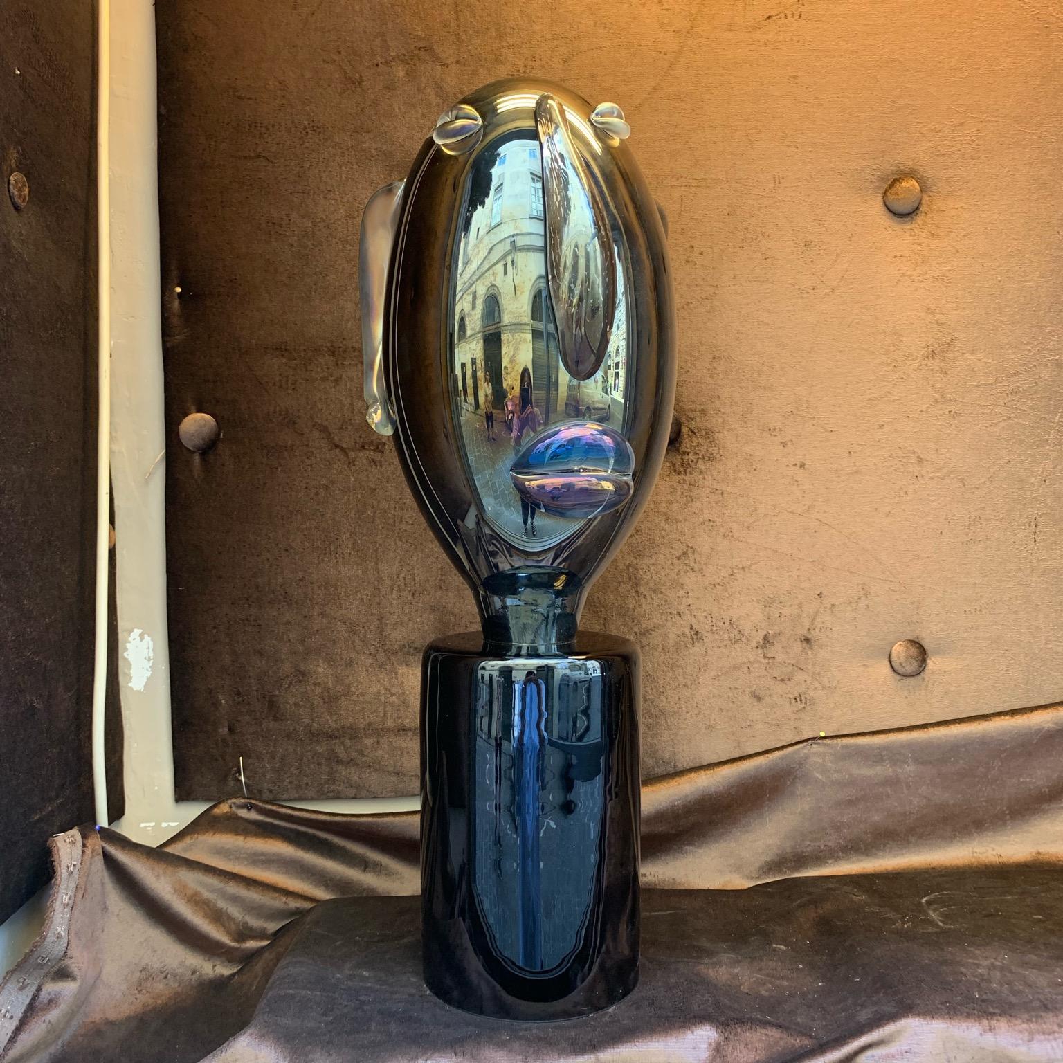 Modernist Murano glass sculpture head shaped Picasso style on black glass round base. The elongated head is in mirrored and iridescent Murano glass. The pair is available. Measurements of the base: diameter cm 17 x height cm 24.