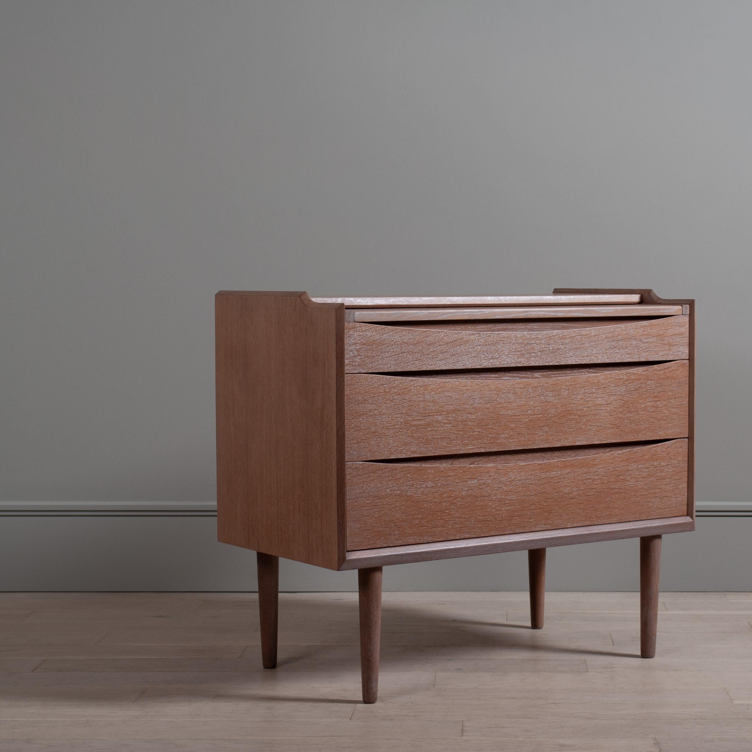 Un mobile modernista scandinavo elegante e multifunzionale. Esterno in Oak con finitura bianca leggermente calcinata. Meravigliose maniglie incassate dalla lunga curva. Diversi usi pratici: cassettiera, scrivania scorrevole e/o vanità con specchio e