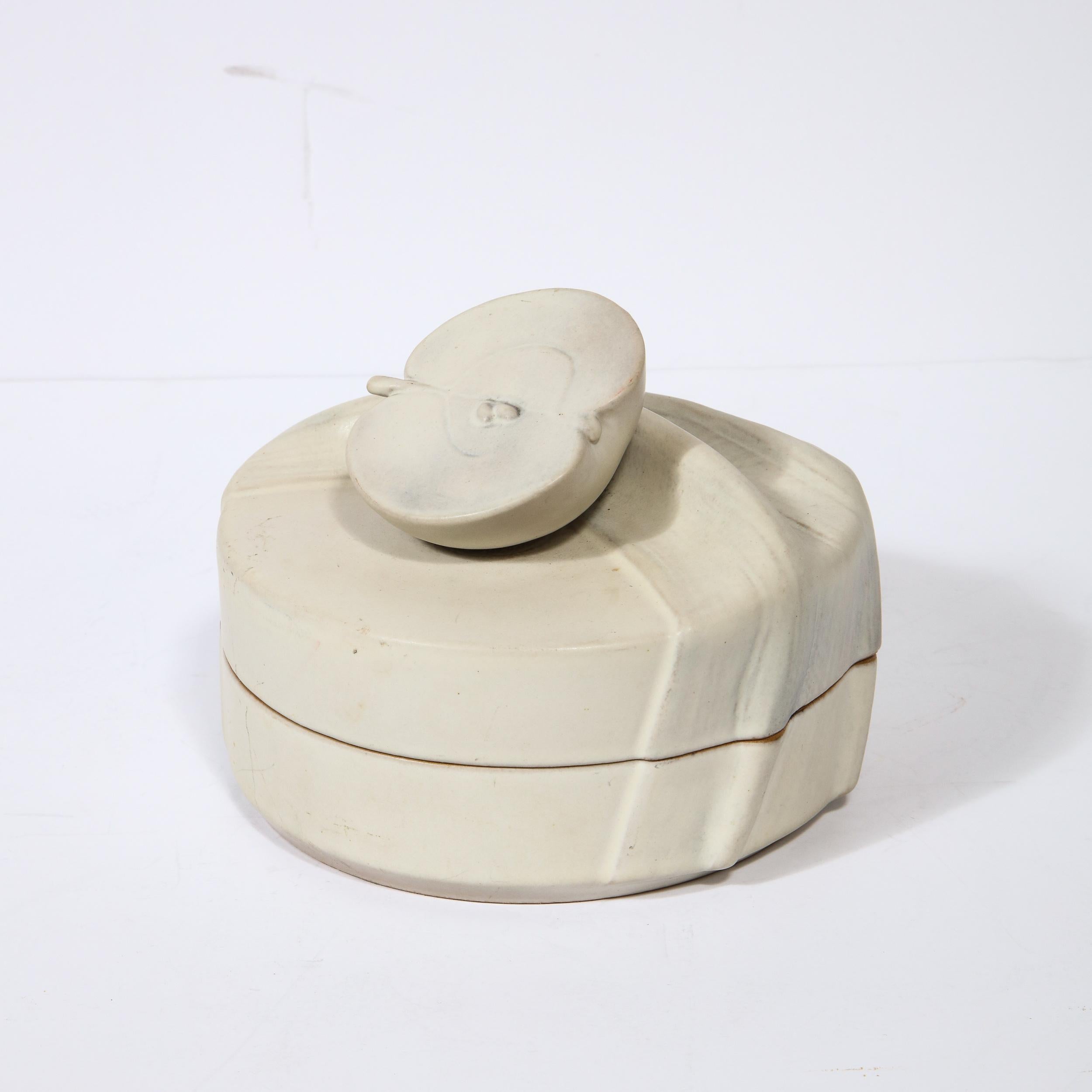 This sophisticated ceramic lidded box was realized by the esteemed maker Rosenthal. It features a round body with a sculptural pull in the form of a halved apple sitting on a textural surface that looks like pulled fabric (a gathered table cloth per