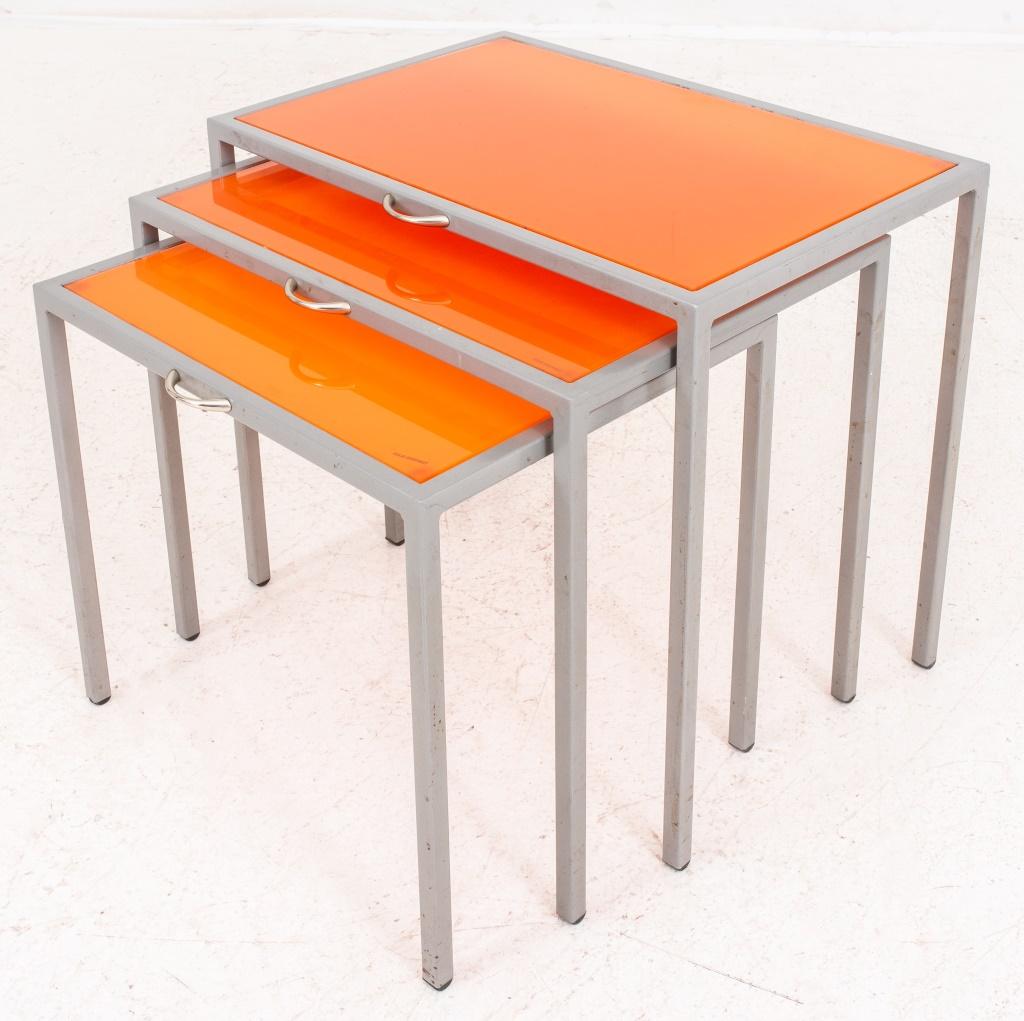 Tables gigognes modernistes en verre orange et acier, 3, chacune rectangulaire avec structure en acier et plateau en verre trempé orange, poignées sur le côté de chaque table. 

Dimensions : 21