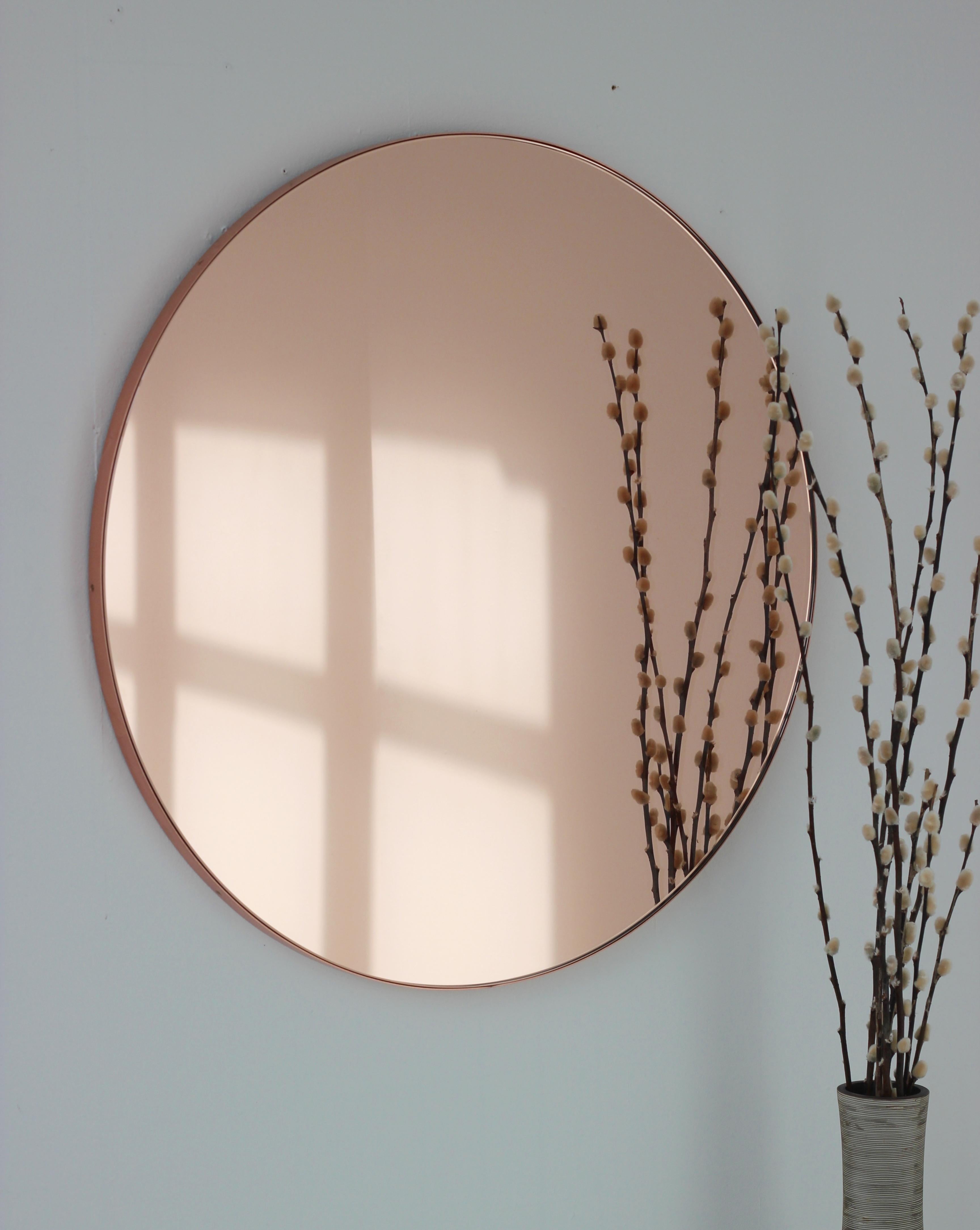 Contemporary Peach / Rose Gold tinted Orbis™ round mirror with a brushed copper frame. The detailing and finish, including visible copper plated screws, emphasise the craft and quality feel of the mirror. Designed and handcrafted in London,