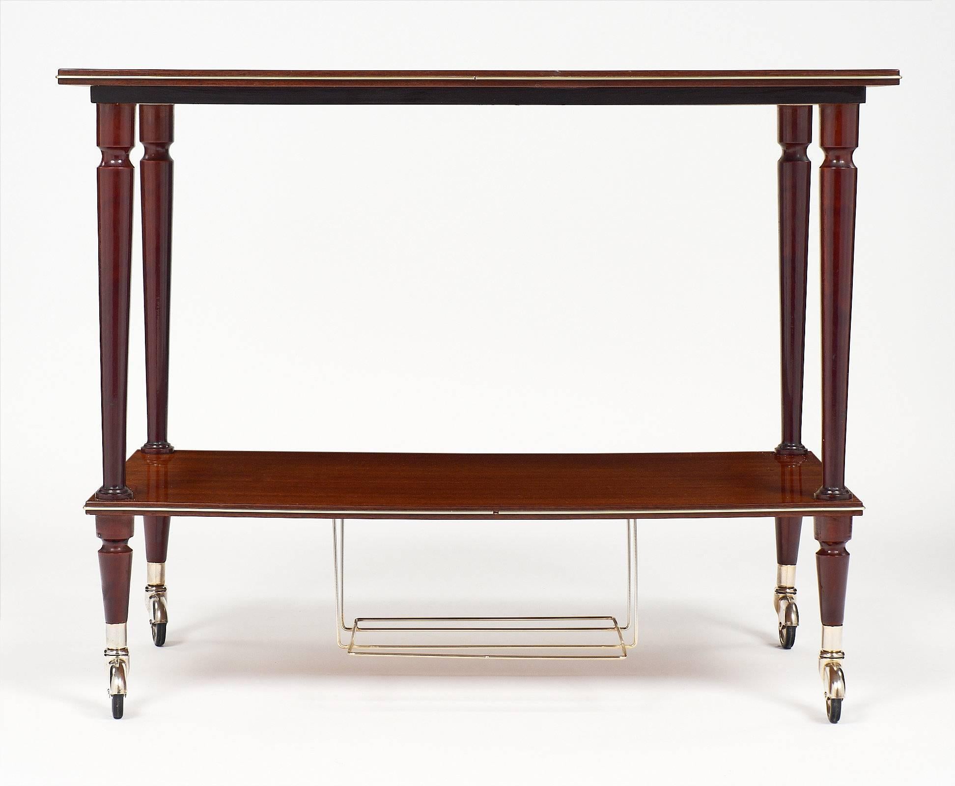 A French modernist period vintage tea cart made of mahogany and brass. This piece could also be used as a side table or bar cart. The tapered legs sit on casters. We love the high gloss finish and the efficiency of this table, right out of “Mad Men.”