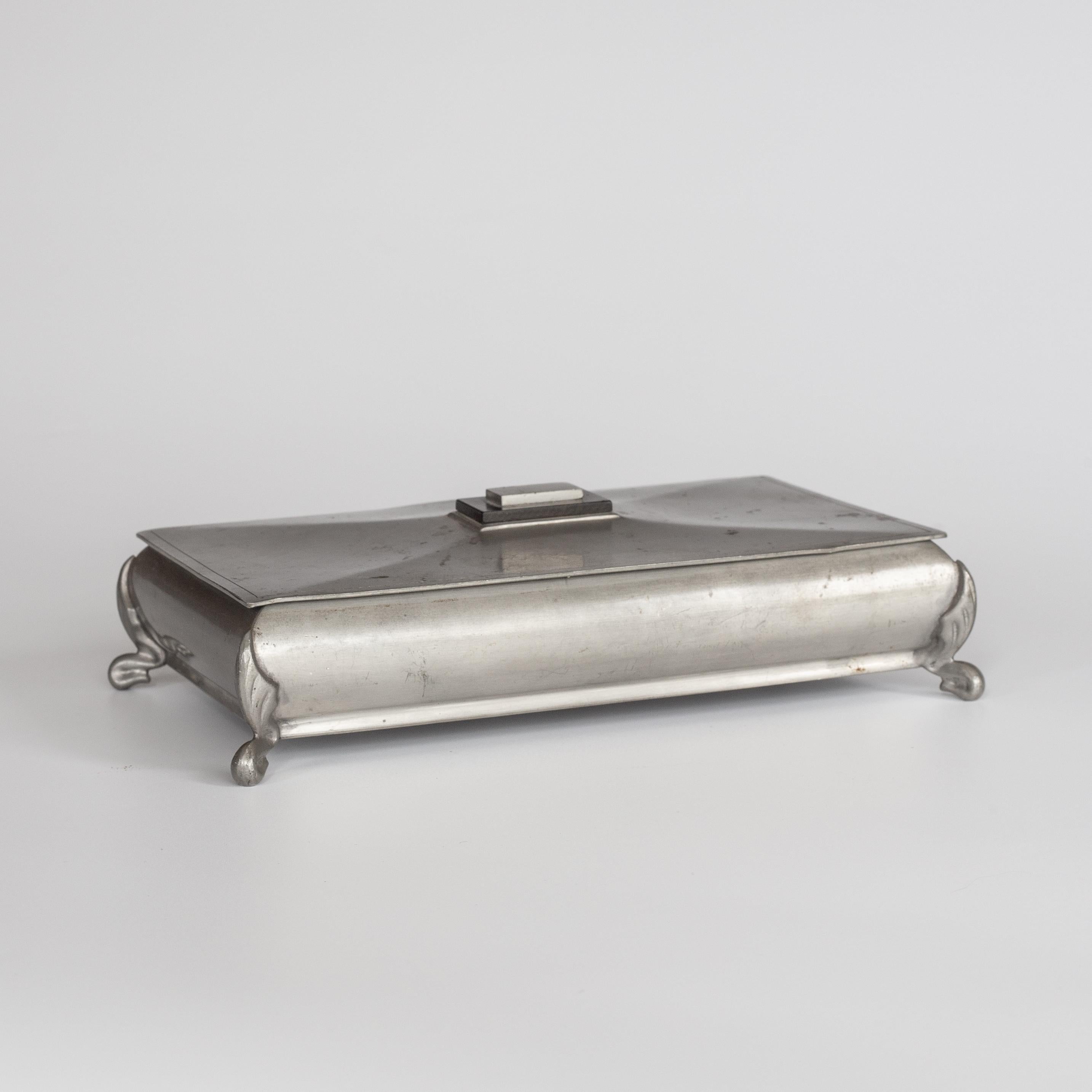 Caja metálica modernista sueca de 1935, que muestra una mezcla perfecta de funcionalidad y elegancia. Fabricada por la renombrada empresa sueca GAB (Guldsmedsaktiebolaget), esta elegante caja de estaño muestra las líneas limpias y los detalles