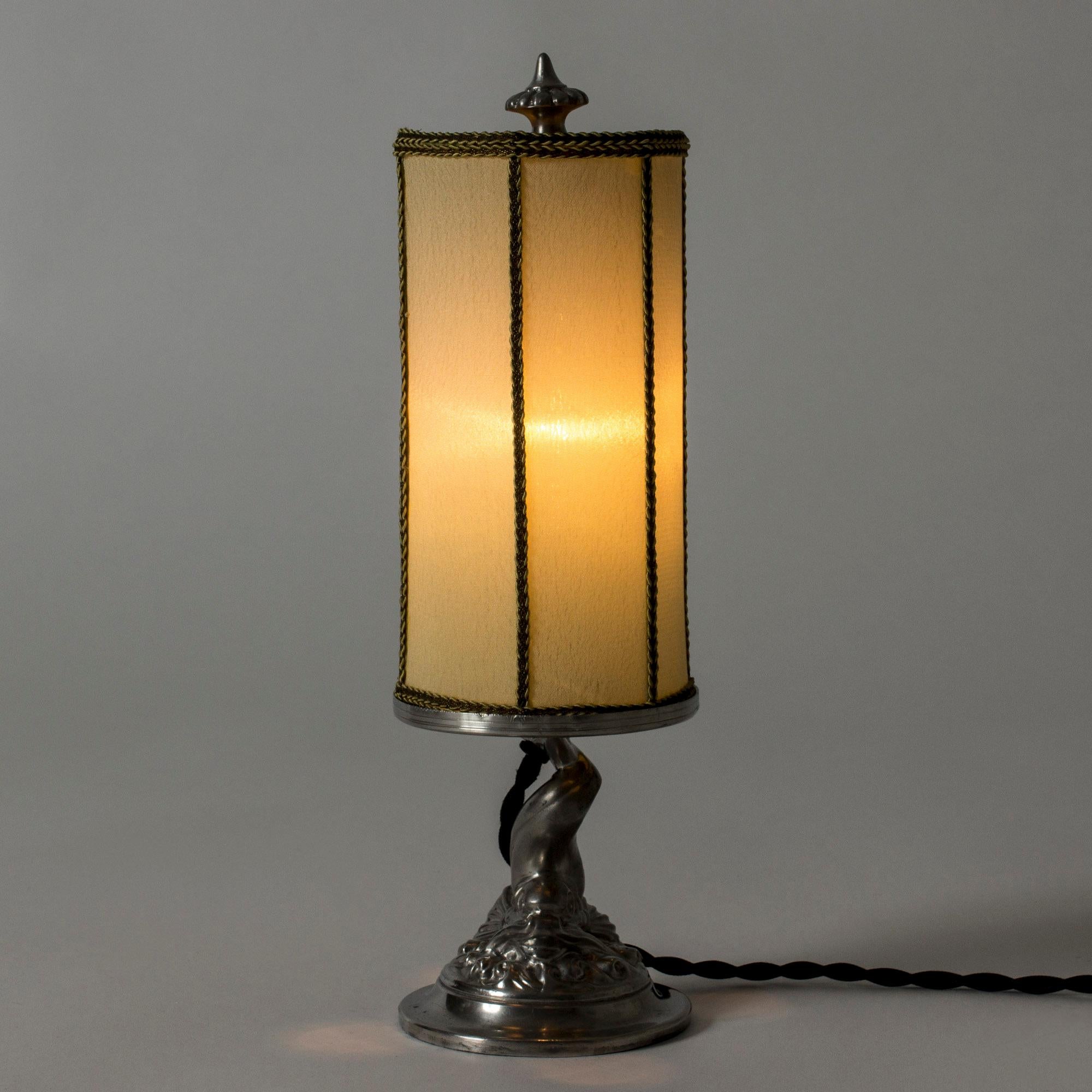 Belle lampe de table des années 1930 de GAB, fabriquée en étain. Base en forme de poisson stylisé dans un tourbillon d'eau. Teinte textile originale.