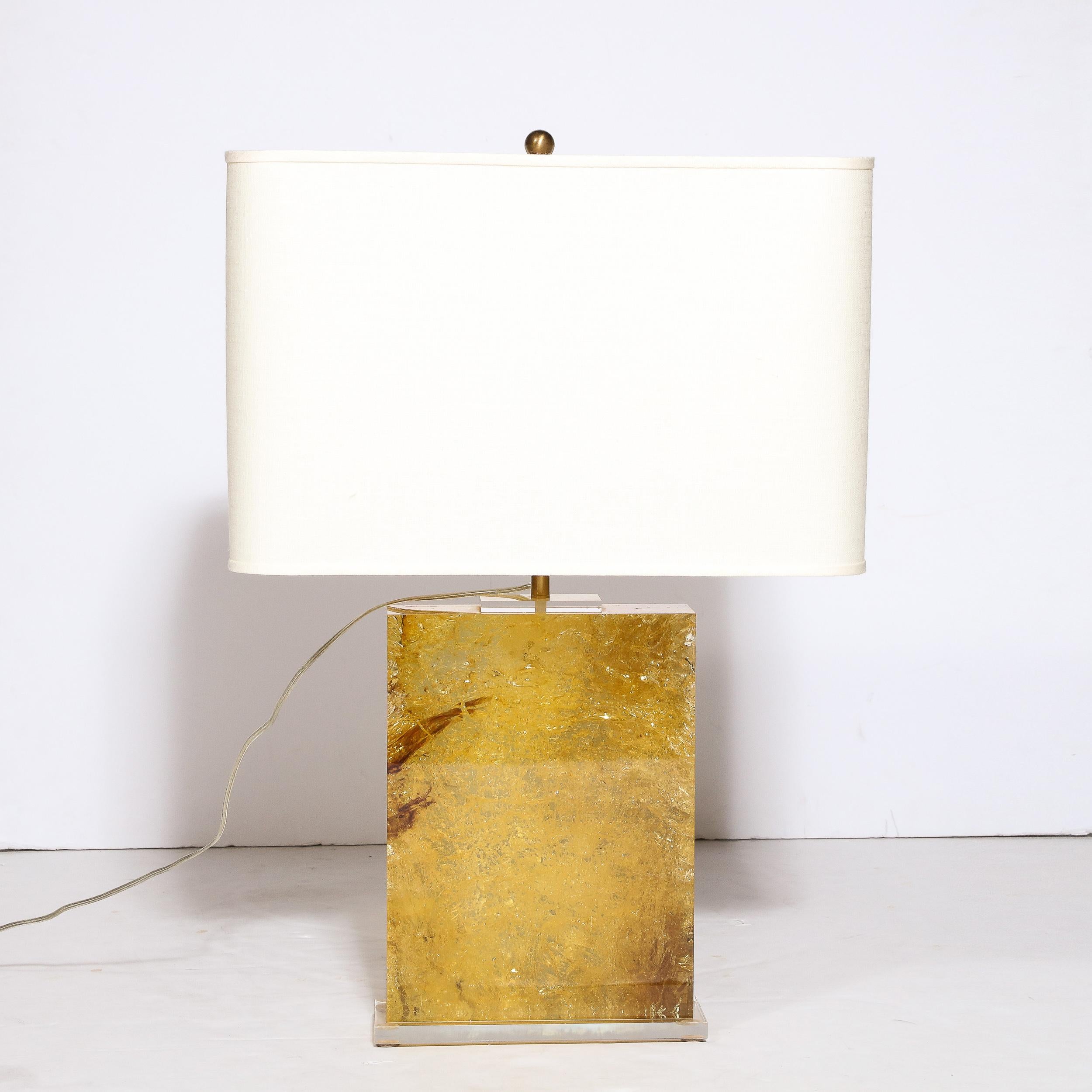 This beautiful modernist pressed lucite table lamp was realized in the United States during the latter half of the 20th century. It features a volumetric rectangular form with an interior full of textural and sumptuous tonalities of gold and amber,