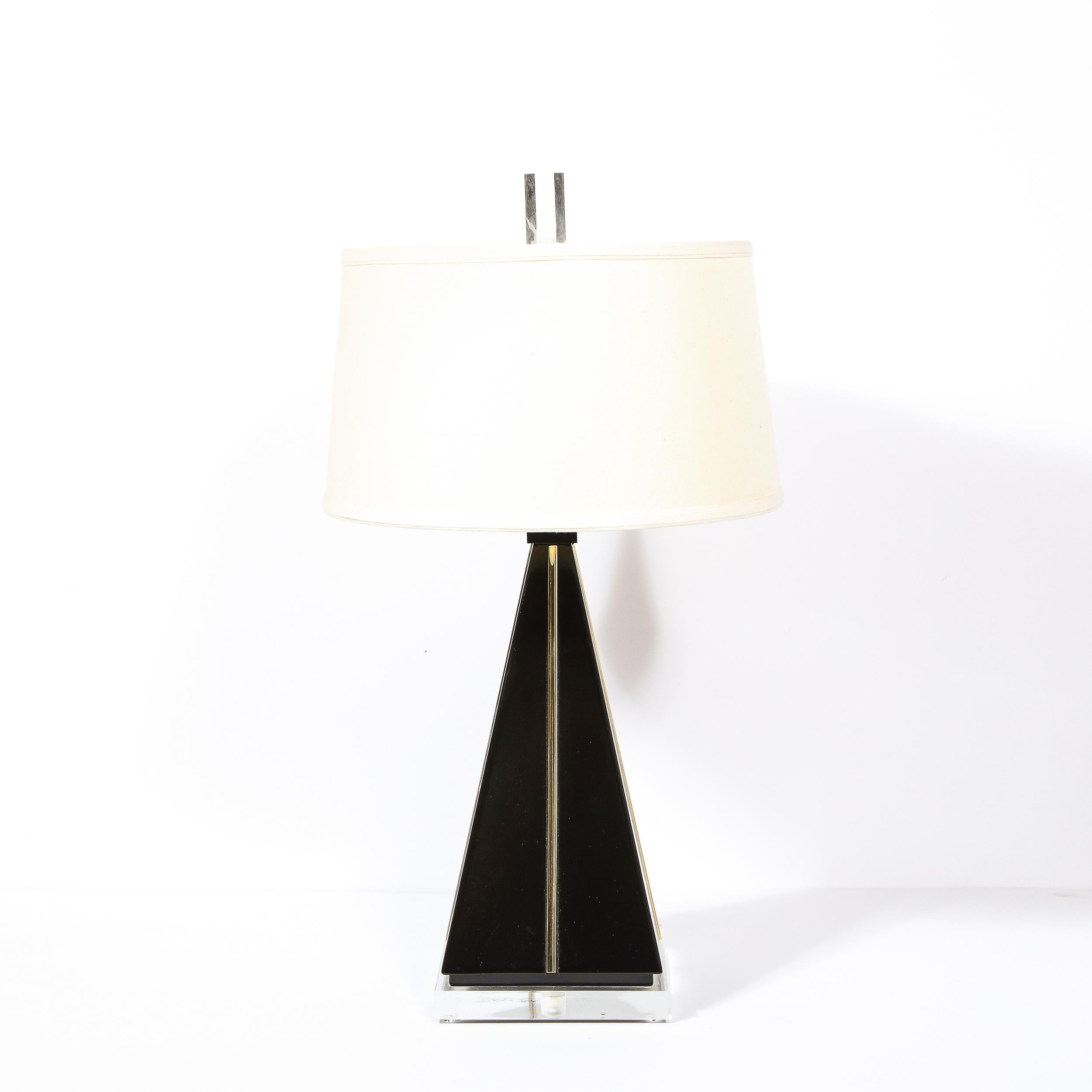 This stunning modernist lamp was realized in the United States, during the latter half of the 20th century. It features a lucite base from which a pyramid body ascends finished in black lacquer with rectilinear gilded resin detailing. The lamp comes