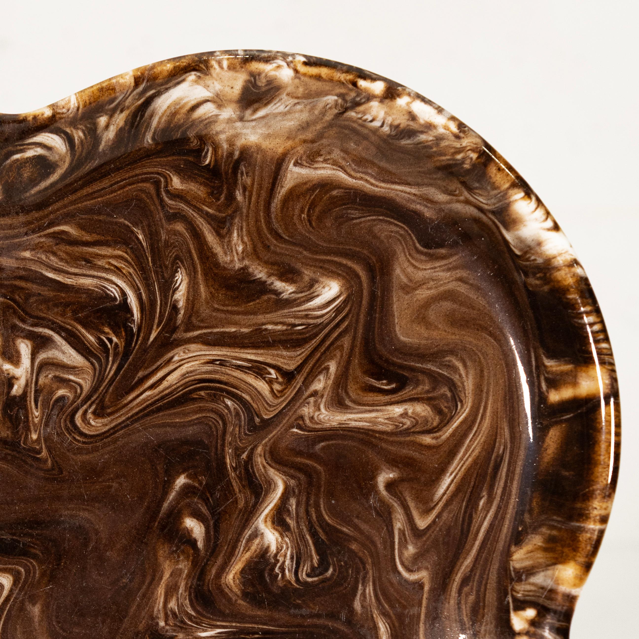 This sculptural modernist ceramic plate features a flowing quatrefoil form and a richly marbled glaze in deep earth tones, including swirls of chocolate brown, tan, and cream. Signed McIntyre, the plate evokes a sense of organic movement and natural