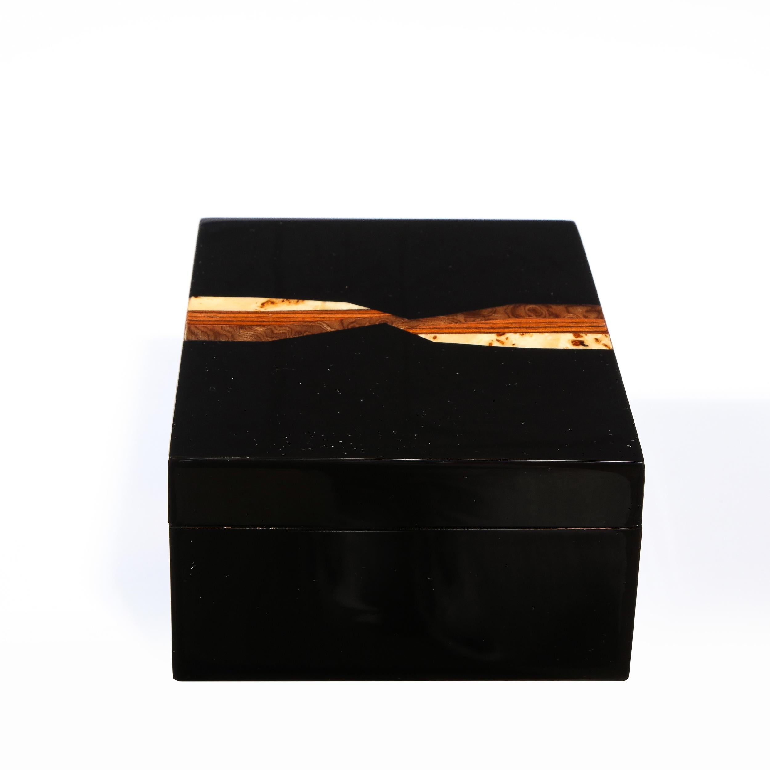 This stunning black lacquer inlaid lidded box was realized in the Philippines during the latter half of the 20th Century. It features a rectangular body with a banded inlay consisting of burled walnut and burled elm separated by a central seam in