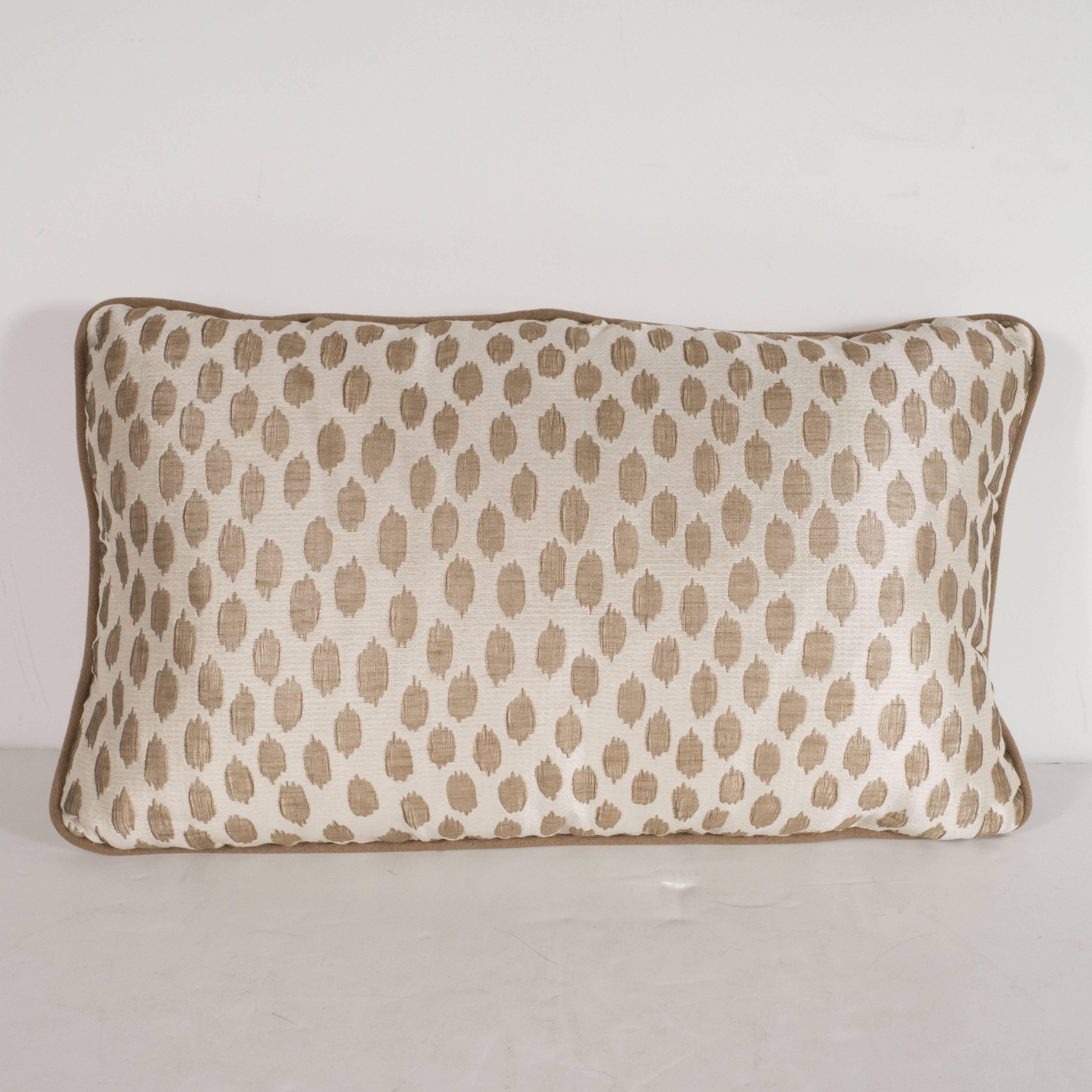 This elegant modernist pillow features organic forms in muted gold hue- with piping in a matching tone- that float against an ecru background with a horizontal weave. With its austere form and sophisticated fabric, this pillow would be a winning