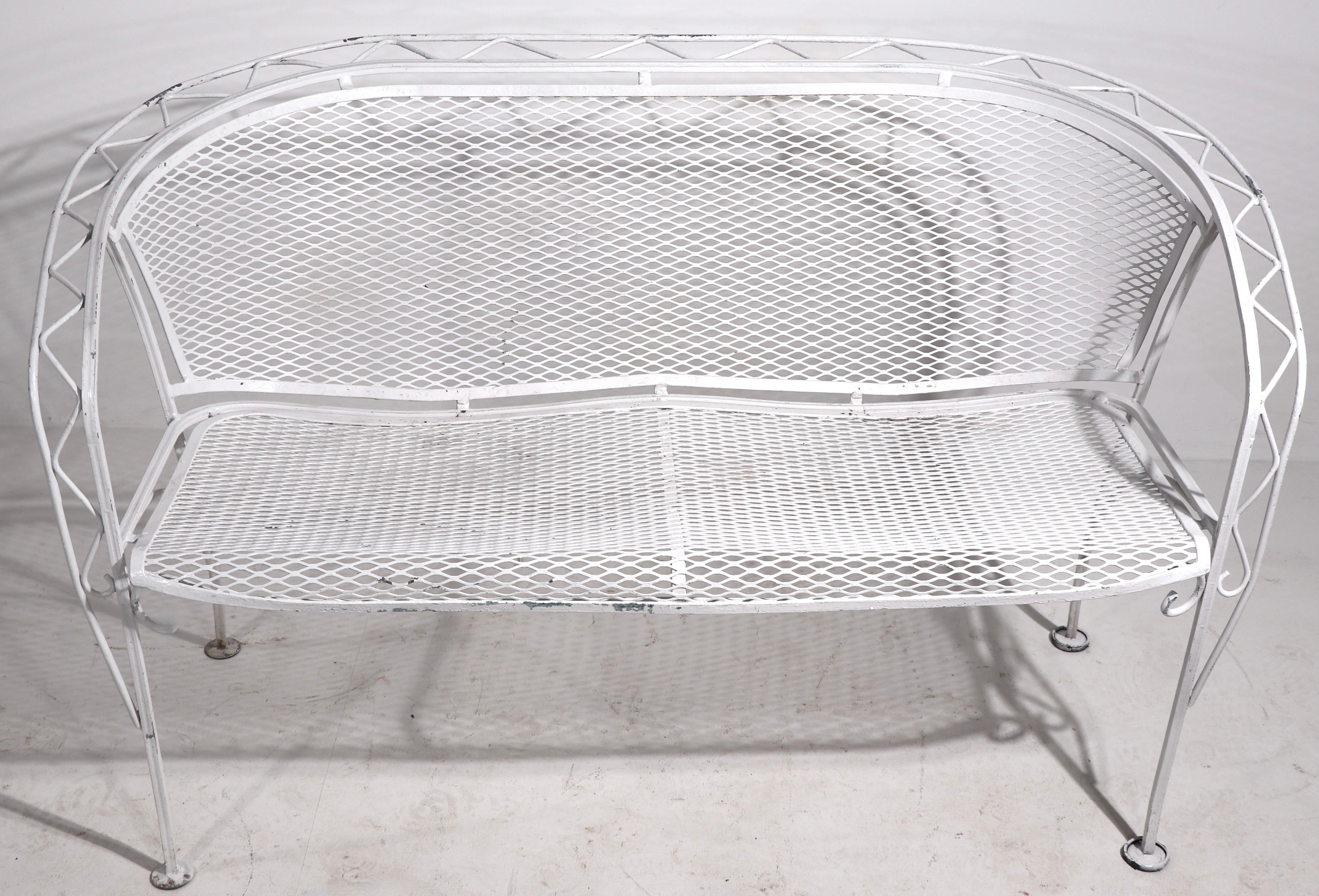 Stylish mid century wrought iron and metal mesh settee by Salterini. This example is in very good condition, free of breaks, bends, or repairs. Currently in later white paint finish which shows some wear and loss, usable as is or we offer custom