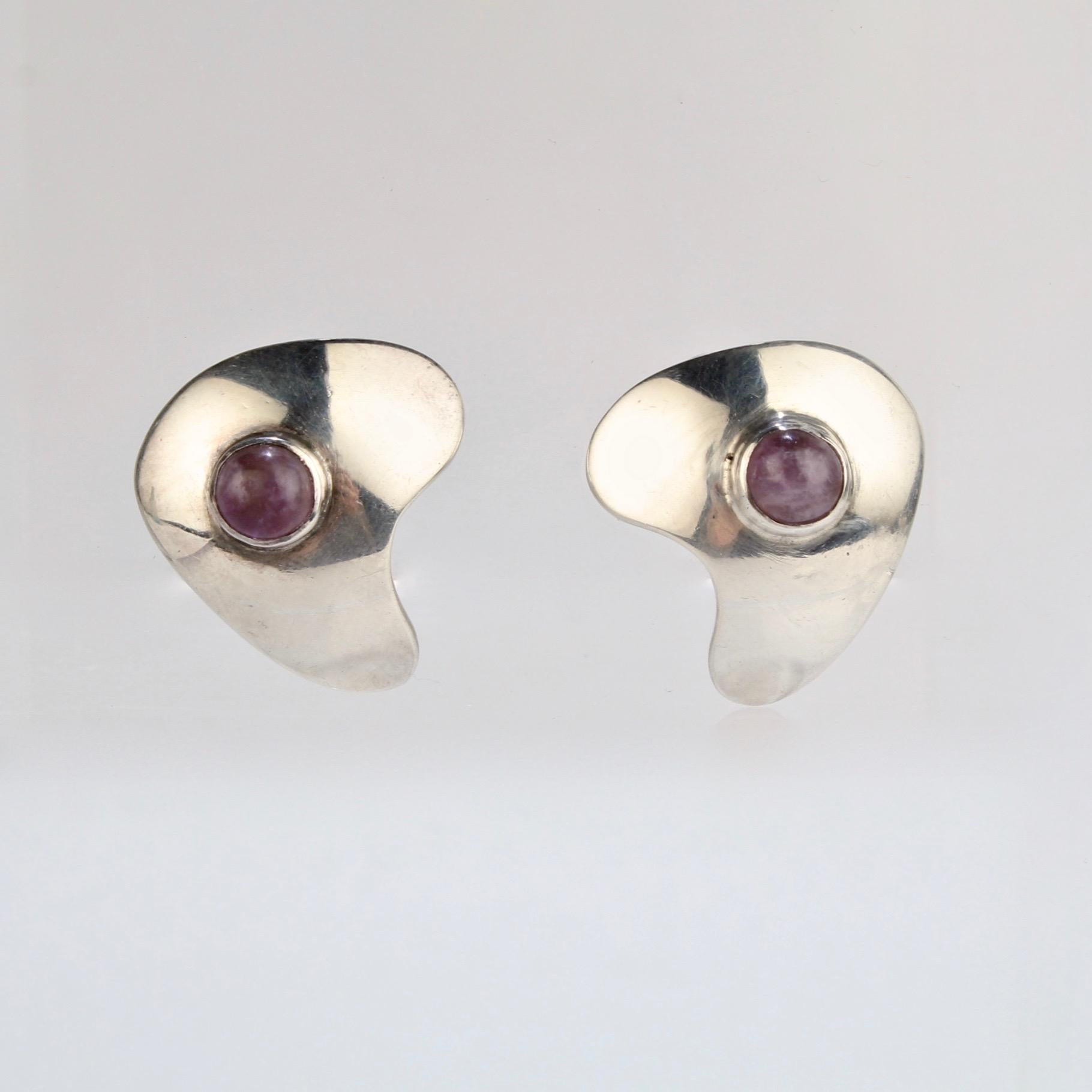 A wonderful pair of Sam Kramer sterling silver and amethyst earrings.

Each abstract, convex earring is bezel set with an amethyst cabochon.

Marked on the reverse with a mushroom mark for Sam Kramer and Sterling.

A great pair of earrings from one