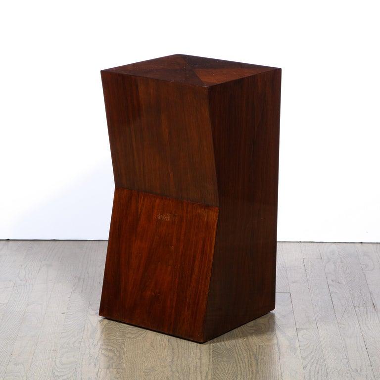 This elegant modernist pedestal was realized in the United States during the latter half of the 20th century. It Composed of bookmatched walnut, the pedestal offers a Minimalist and austere volumetric rectangular form with angular concave cut out on