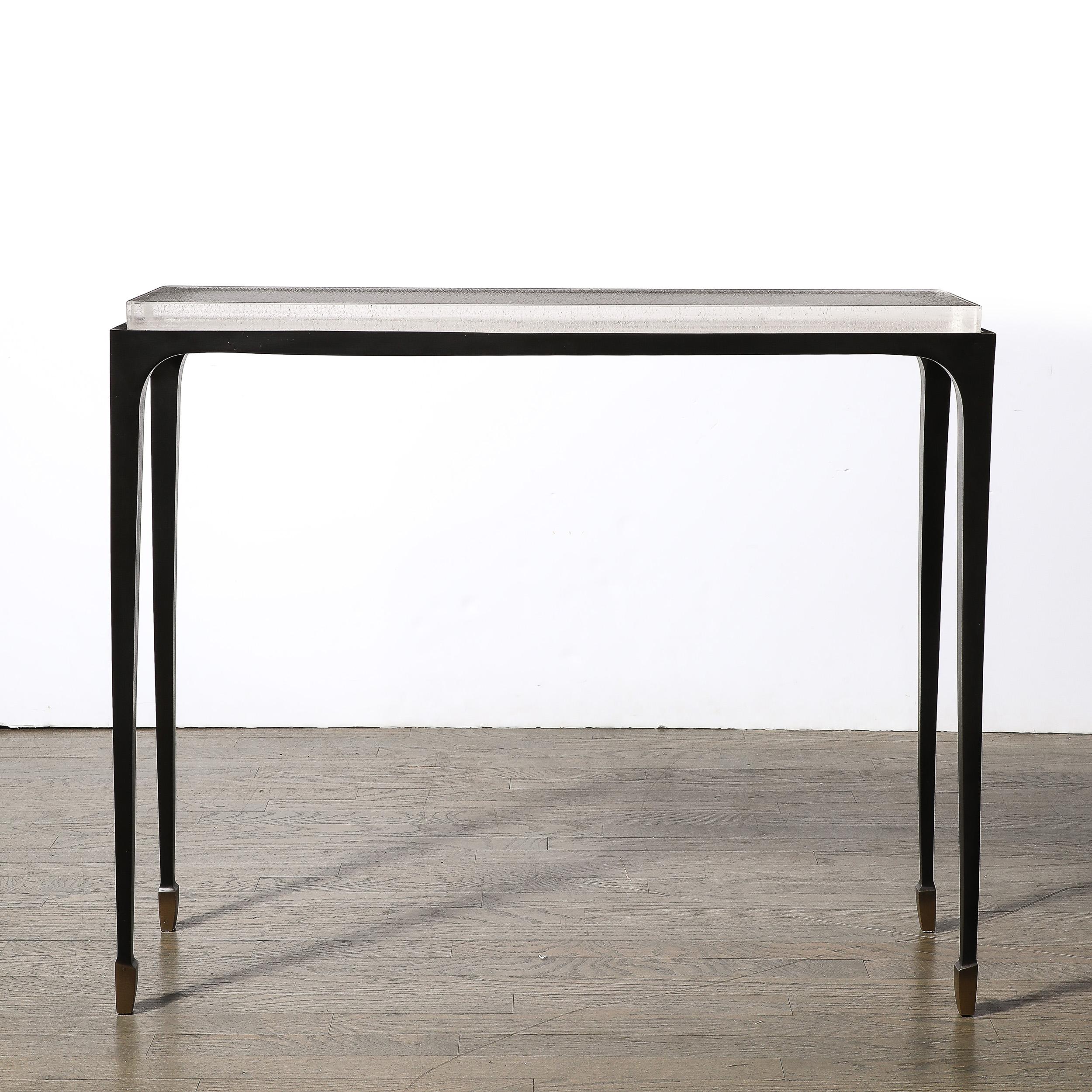 This highly sleek and elegant Modernist Sculptural Bronze and Inset Caste Ice Glass Console Table W/ Exposed Integral Brass Sabots is by Holly Hunt and originates from the United States, Circa 2010. The frame of the table is formed in bronze, with